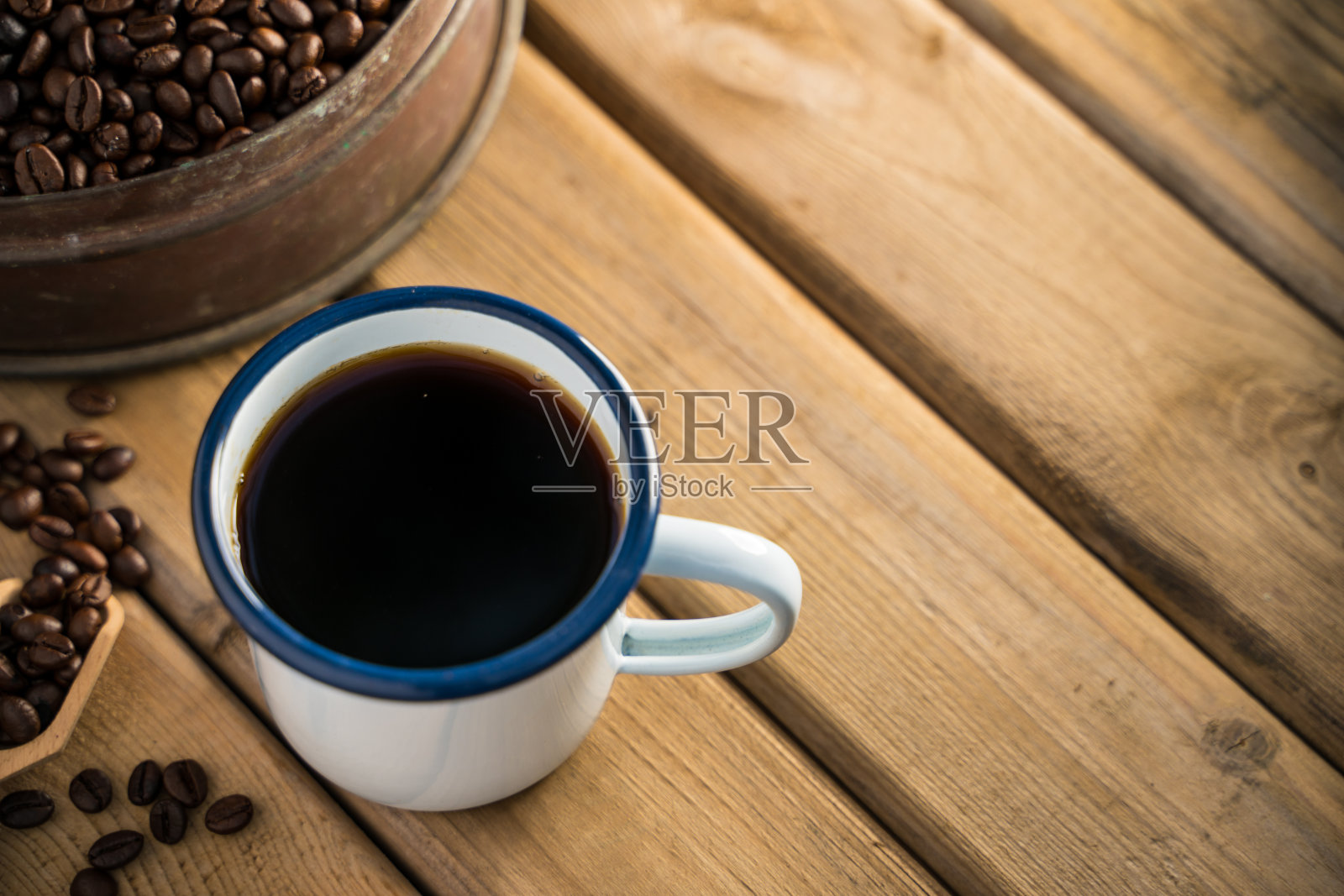 旧木地板上的白色搪瓷咖啡杯和黑咖啡豆。软的焦点。浅聚焦效果。照片摄影图片