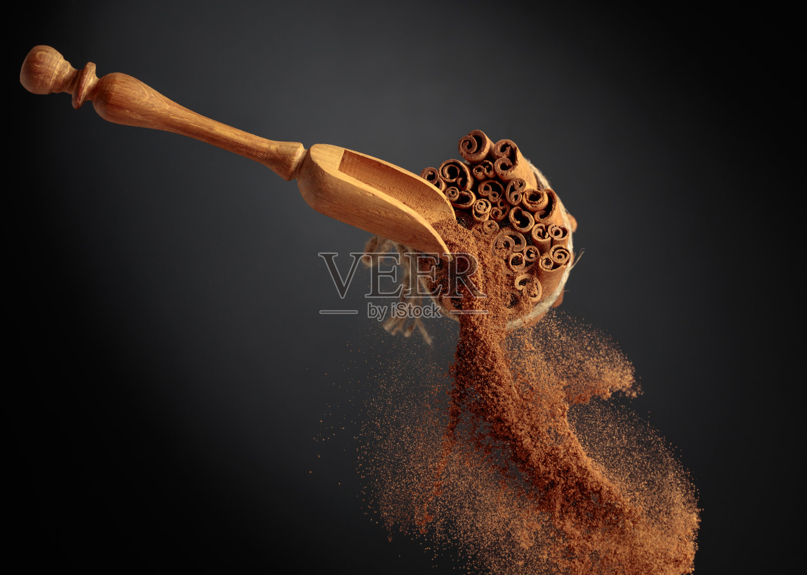 肉桂粉从木勺里倒出来。照片摄影图片