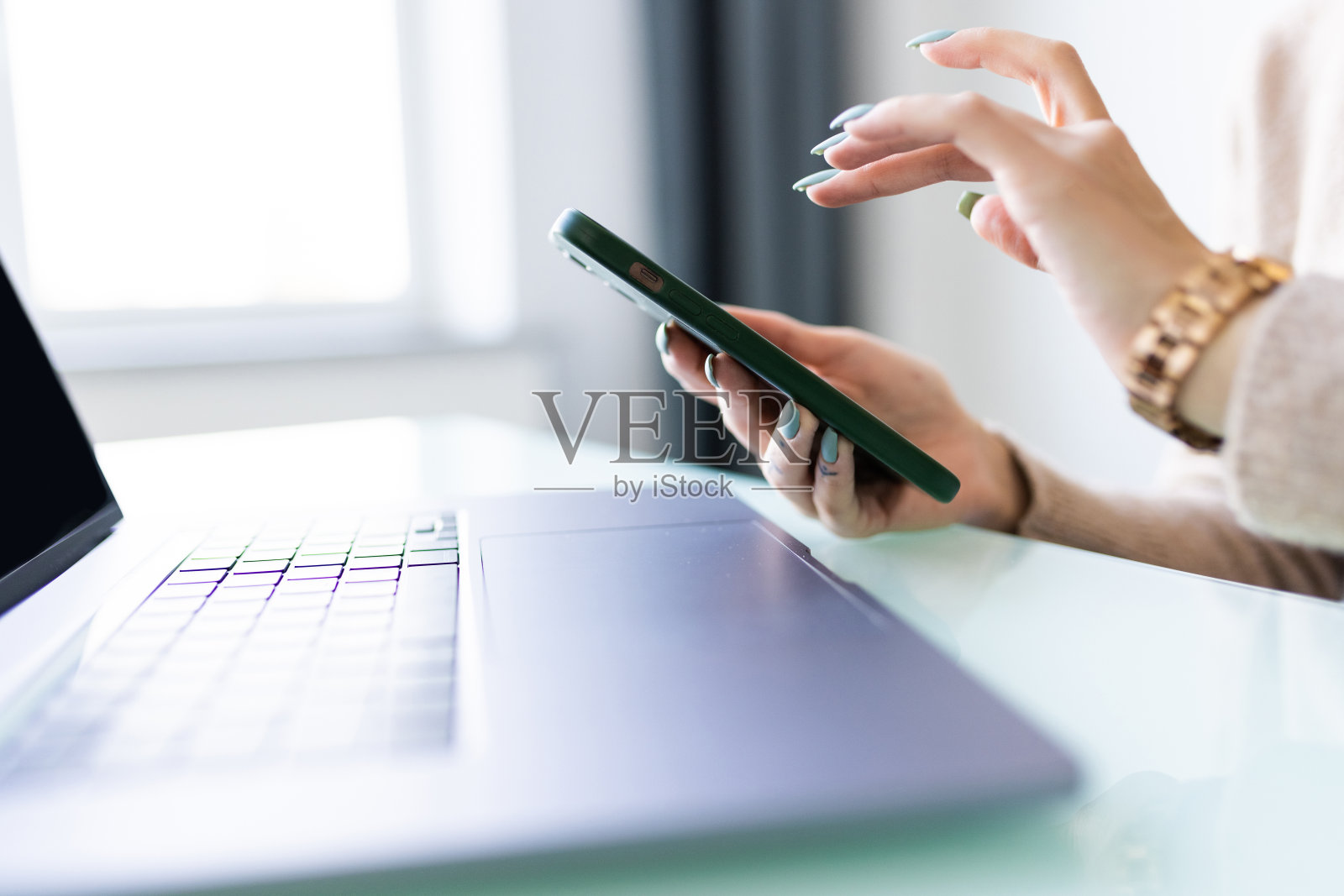 特写年轻女子的手在家里使用笔记本电脑查看智能手机照片摄影图片