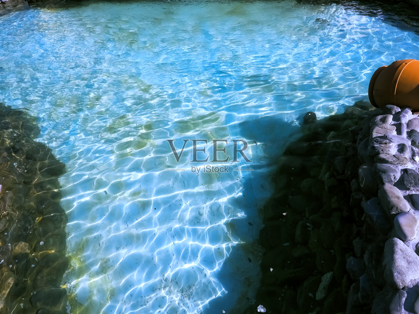 蓝色的夏季装饰池，透明的水在阳光下闪闪发光，石质的侧面照片摄影图片