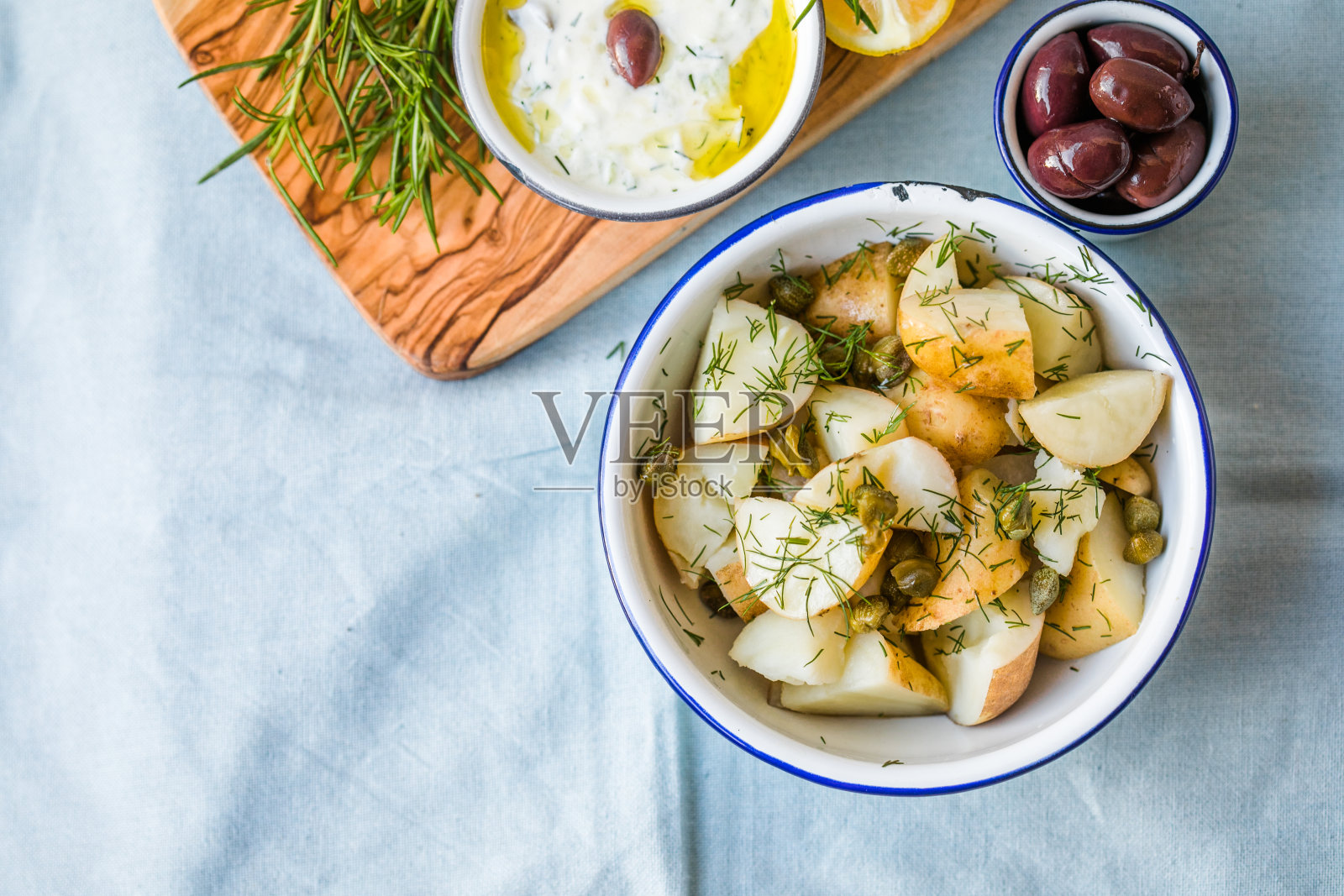 蓝色底色的碗里有莳萝和橄榄的土豆沙拉。健康食品，素食和精益食谱。照片摄影图片