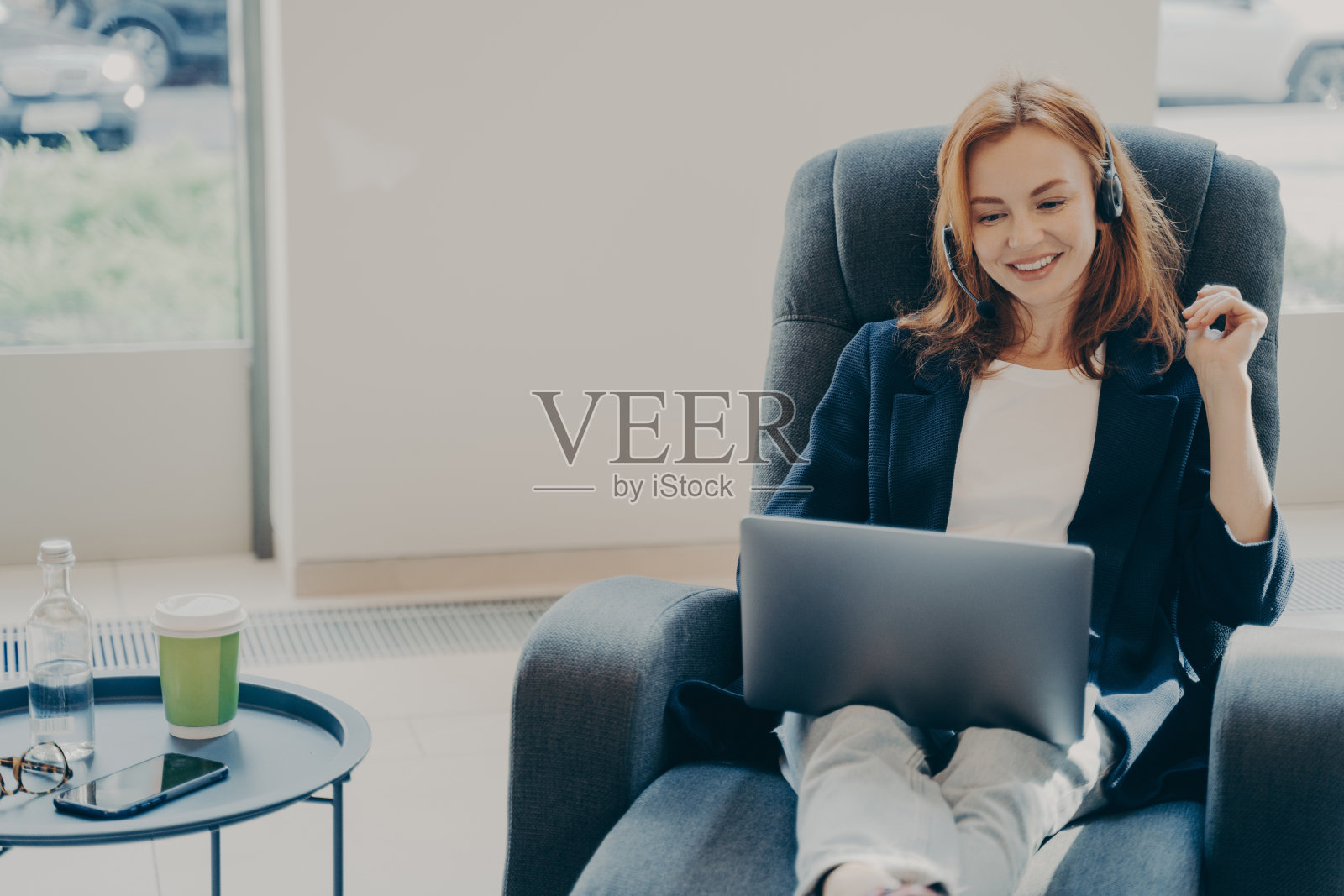 快乐的红发女性自由职业者在耳机与客户沟通在笔记本电脑视频通话照片摄影图片