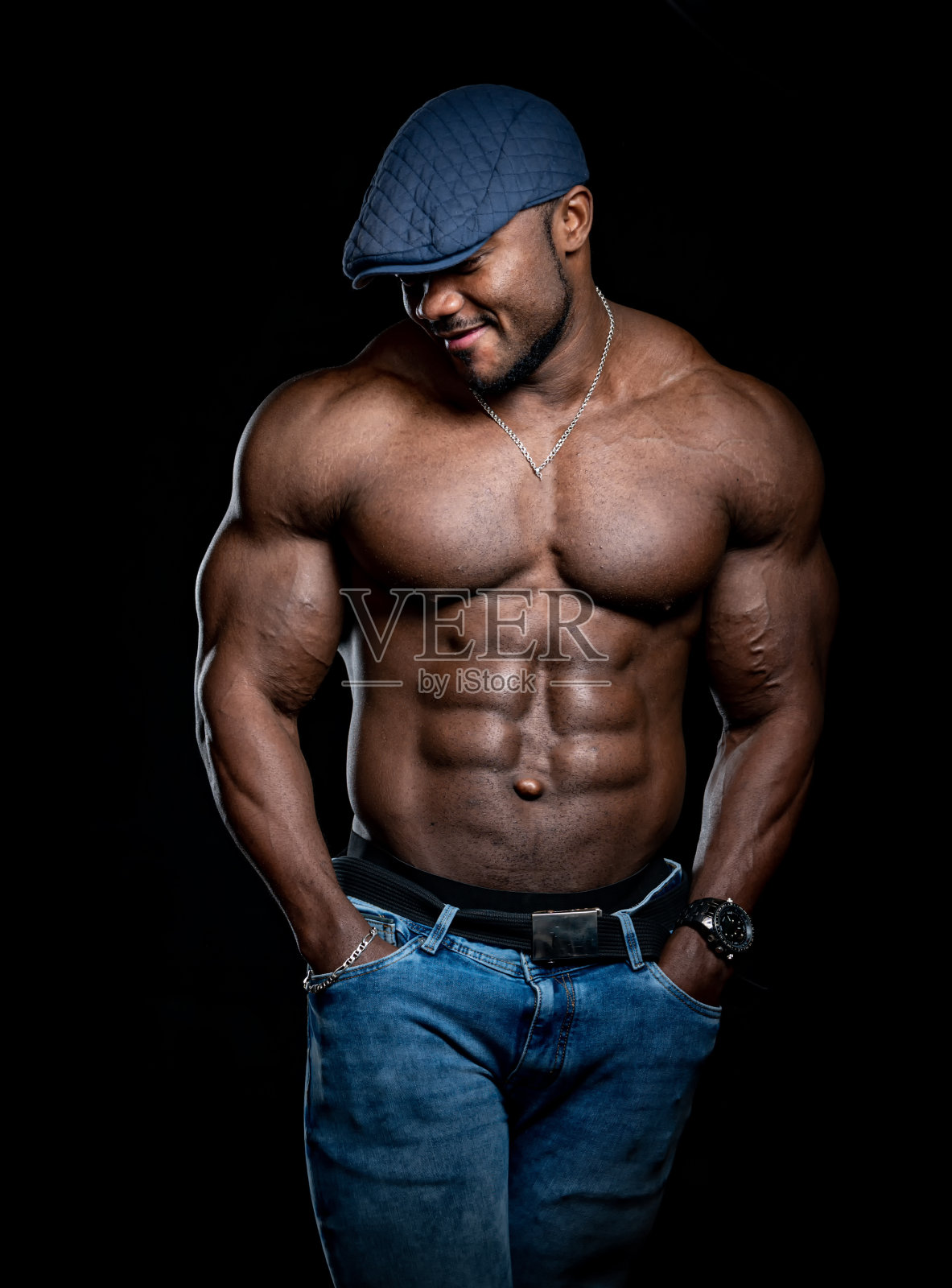 戴蓝帽子的非洲裔美国运动员站着，双手插在口袋里。非常强健的身体和强壮的腹肌。照片摄影图片