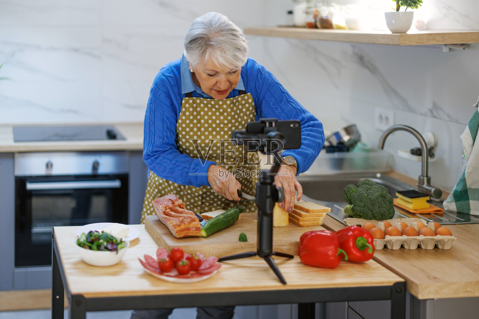 妇女准备食物配方，同时在线流与移动智能手机摄像头为网络厨房大师班频道照片摄影图片