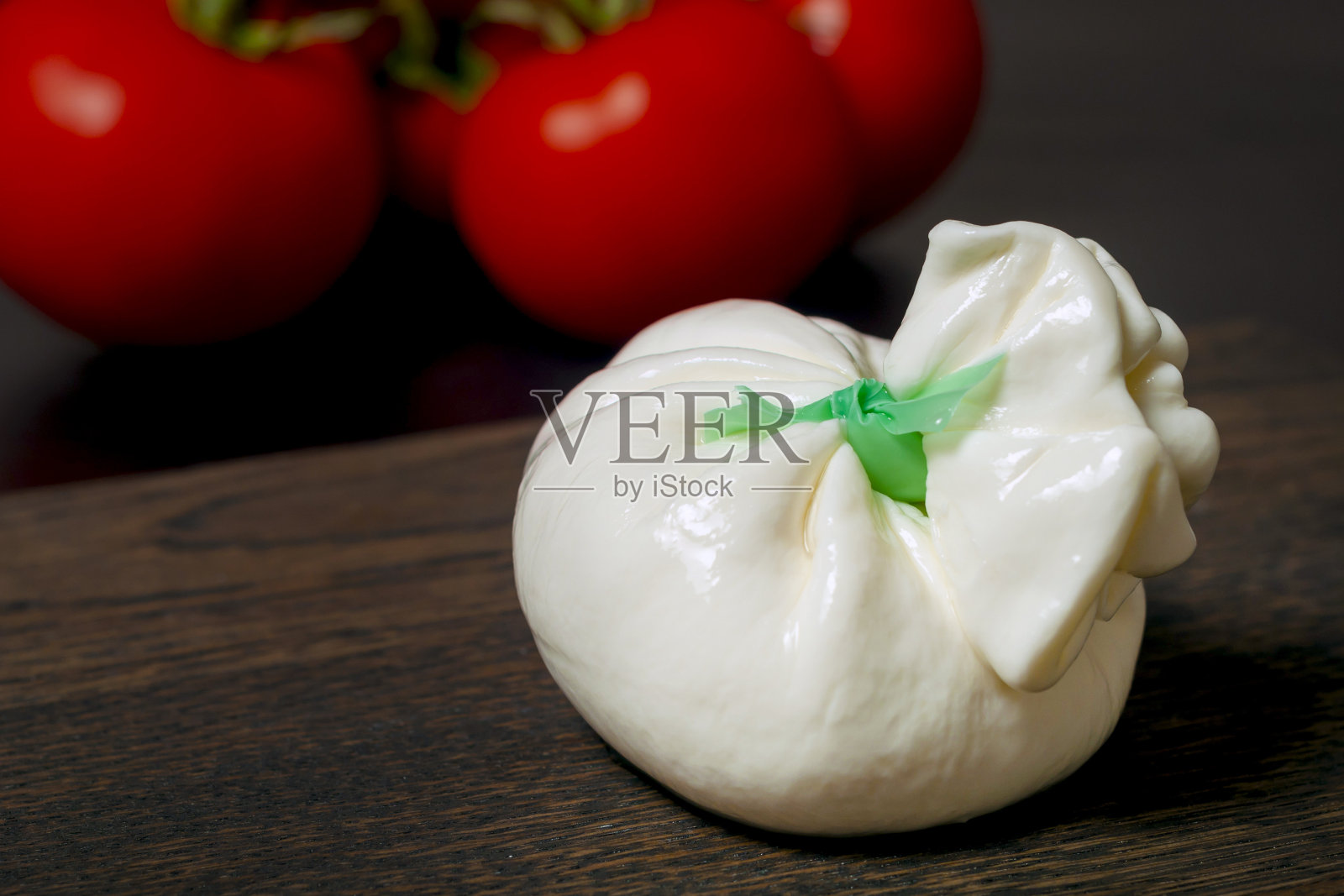 木板上放着意大利布拉塔奶酪，背景是红色的西红柿。照片摄影图片