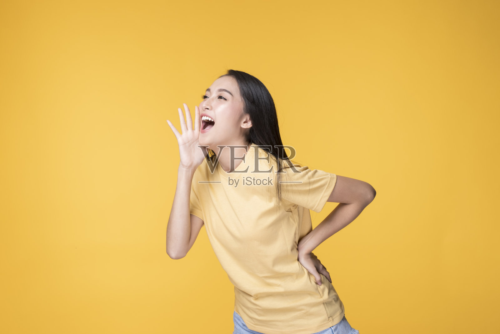 快乐的亚洲女人穿着黄色t恤站在黄色的背景。照片摄影图片
