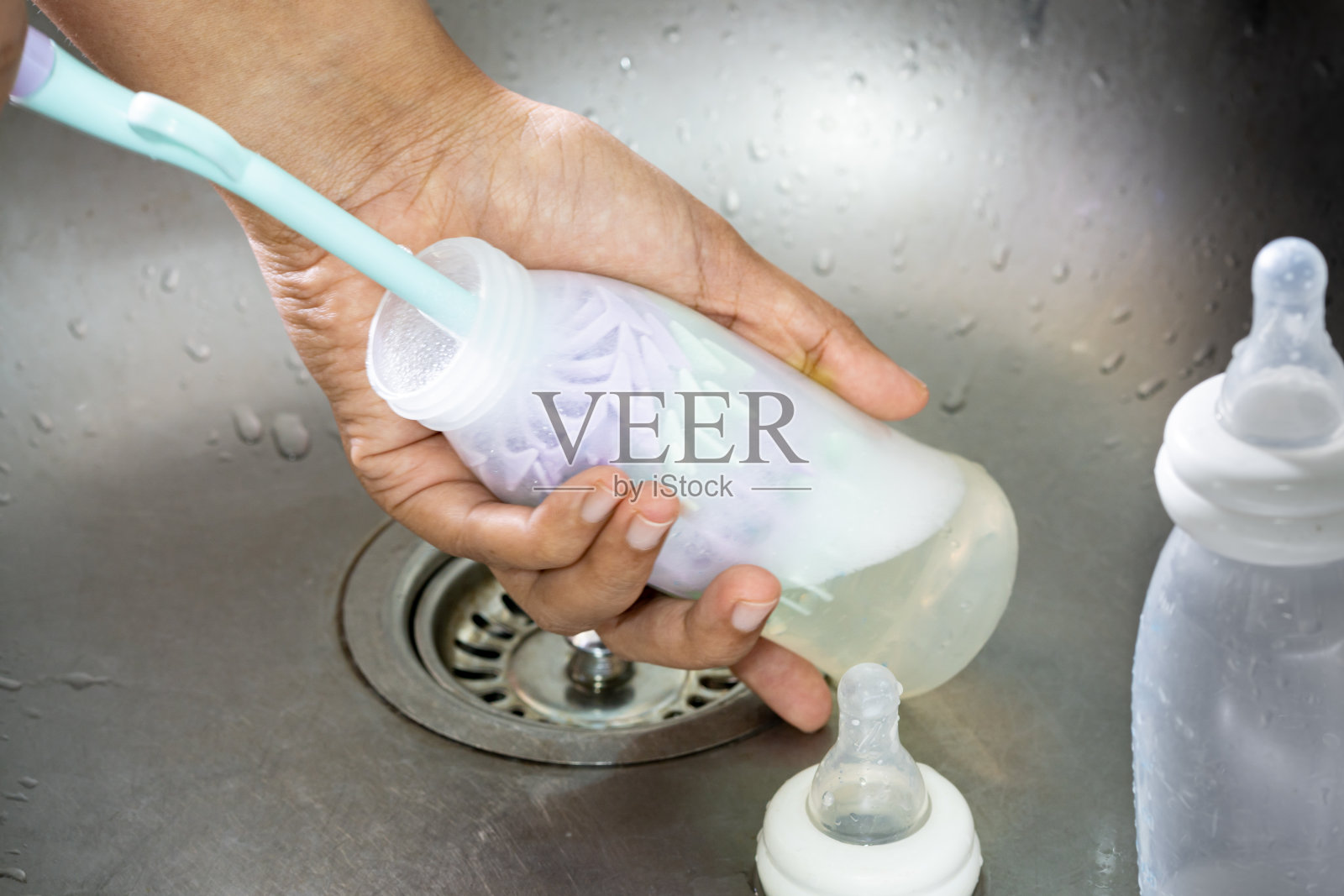 母亲用洗瓶器清洗婴儿的奶瓶，并用洗瓶器旋转清洗奶瓶。照片摄影图片