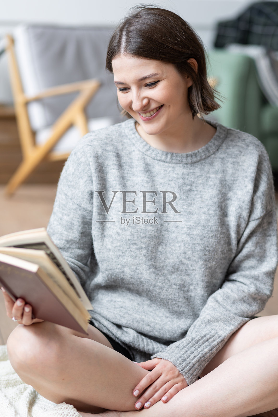 美丽的年轻女子在家里客厅的地板上悠闲地看书。日光。女性在灰色毛衣填充舒适在她的房子。周末照片摄影图片