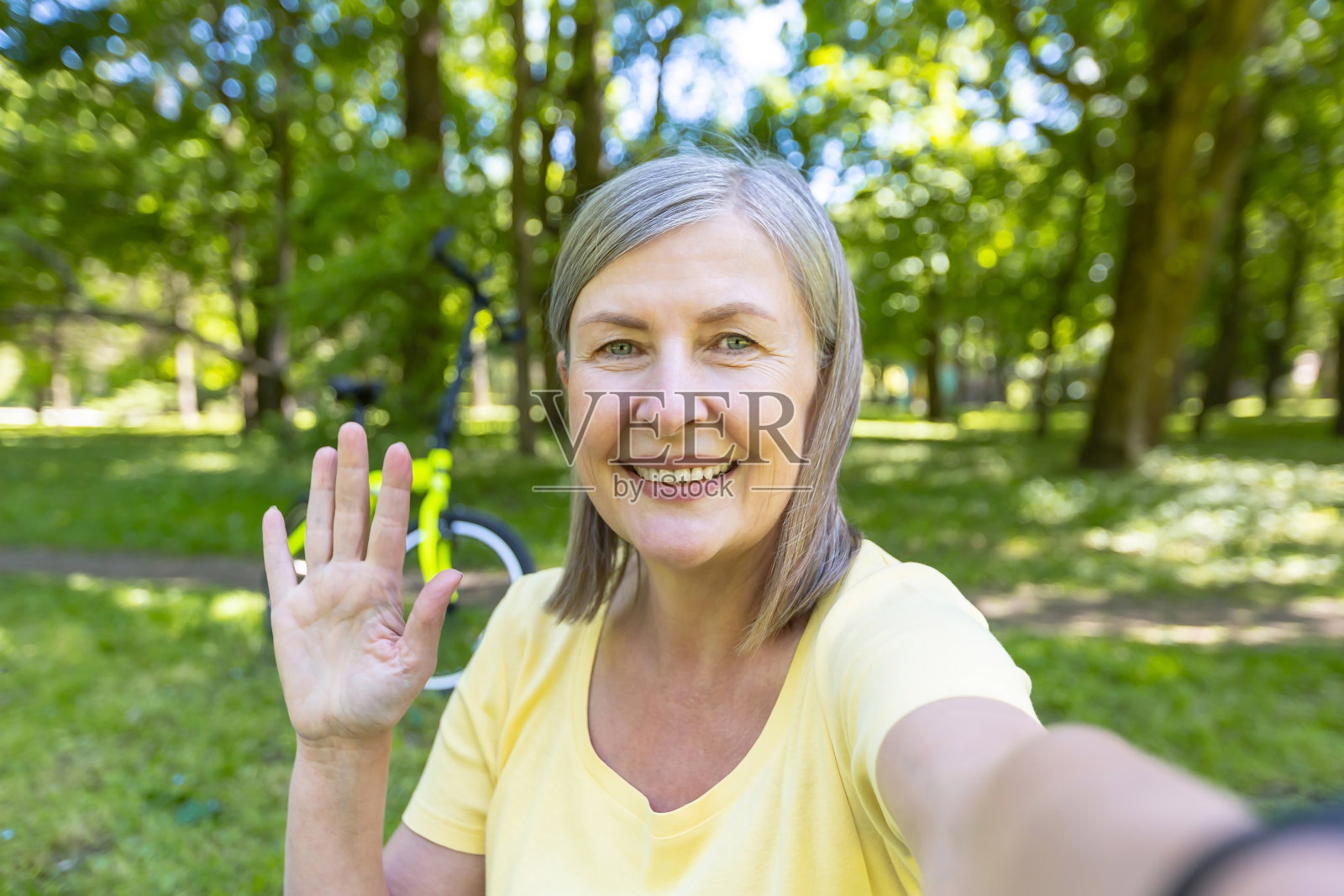白发苍苍的老女人，活跃的女运动员在夏天的公园里看着手机摄像头，微笑着在视频通话中挥手照片摄影图片