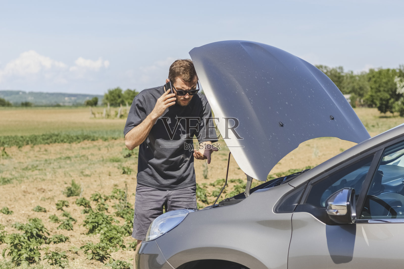 一名男子站在一辆破车旁，用手机打电话。照片摄影图片