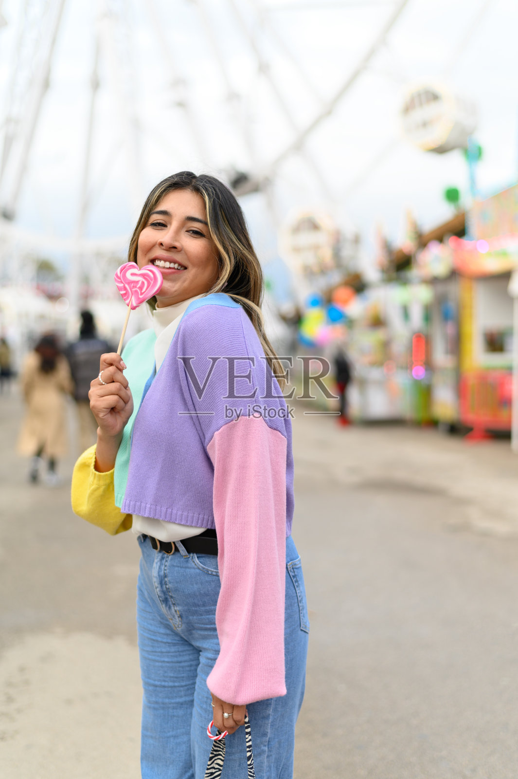 美丽的女人正在游乐园快乐地吃棒棒糖。照片摄影图片