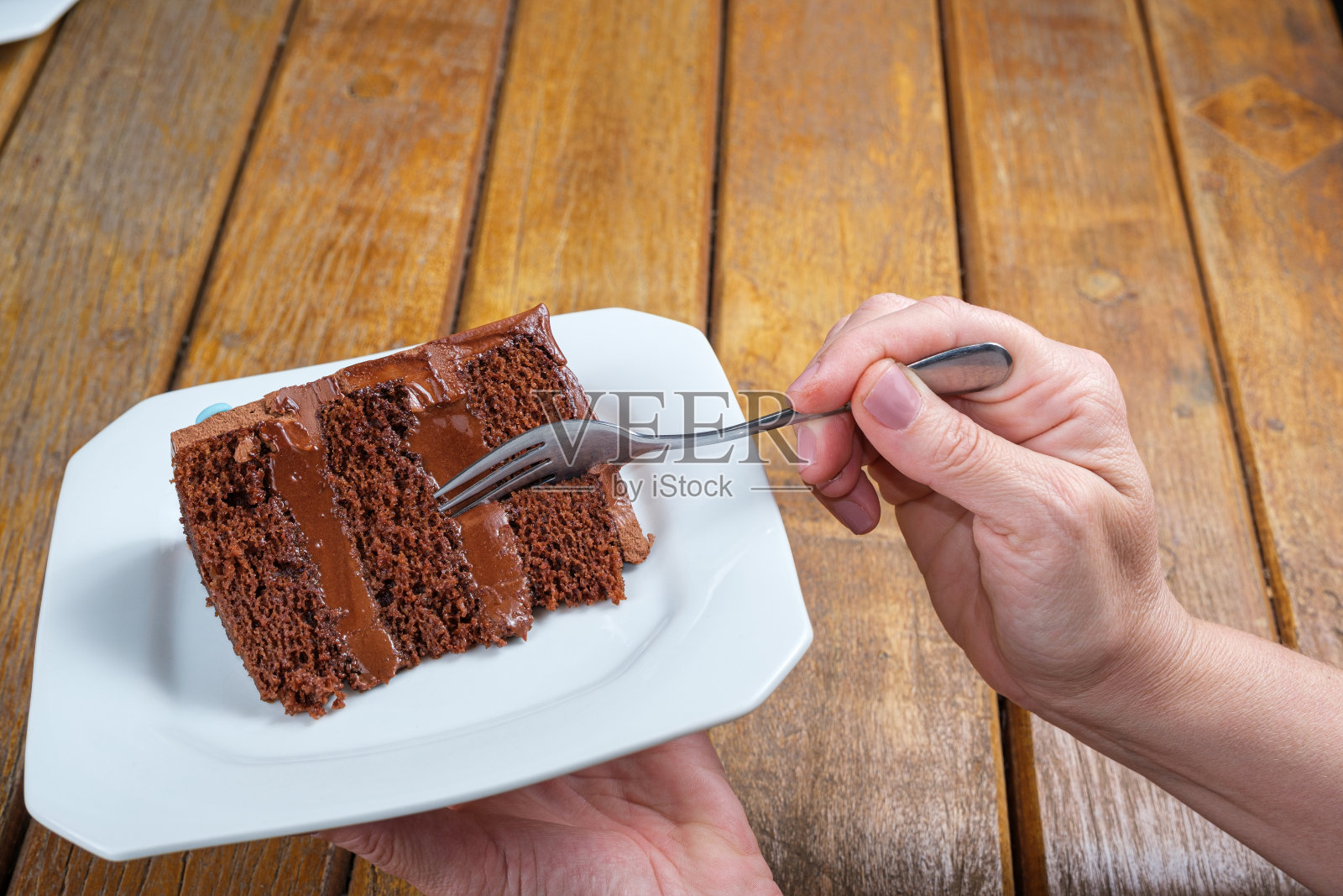女人拿着一个盘子，拿着一块巧克力蛋糕，里面有半甜的巧克力甘纳许。照片摄影图片