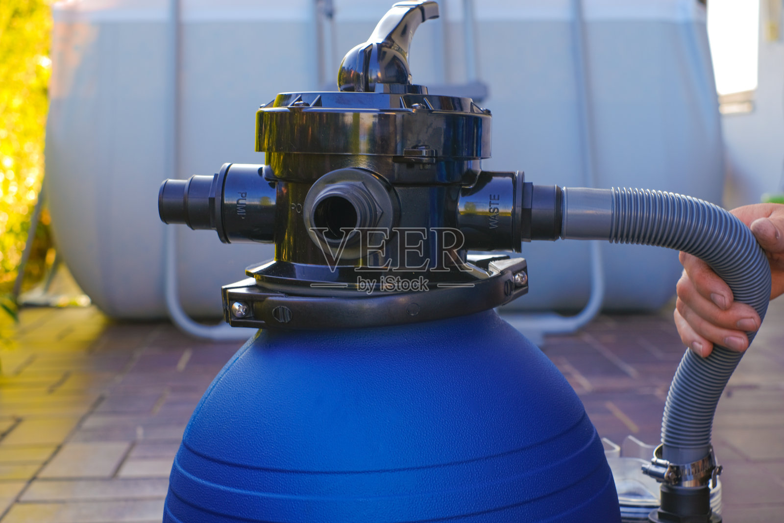 游泳池清洁设备。房子附近的阳台上，一个男人手里拿着蓝色的水过滤器。一名男子把水管挪到游泳池的过滤器旁。照片摄影图片