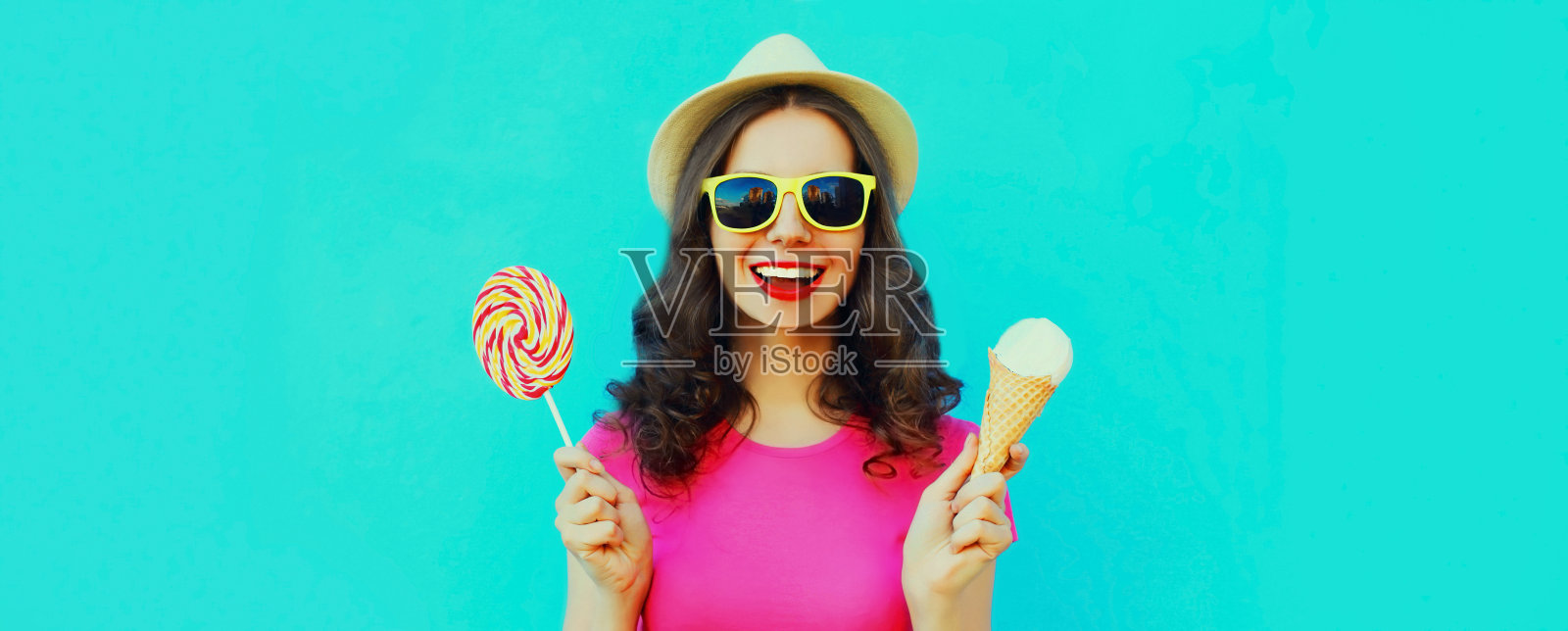 肖像快乐的笑年轻女子与冰淇淋和棒棒糖戴夏天草帽的蓝色背景照片摄影图片