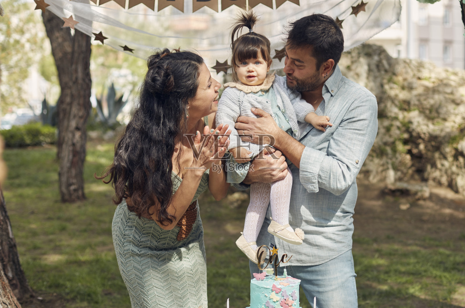 图为，在花园中为小女儿庆祝生日的父母们，正把女儿抱在怀里，假装一个幸福的家庭。照片摄影图片