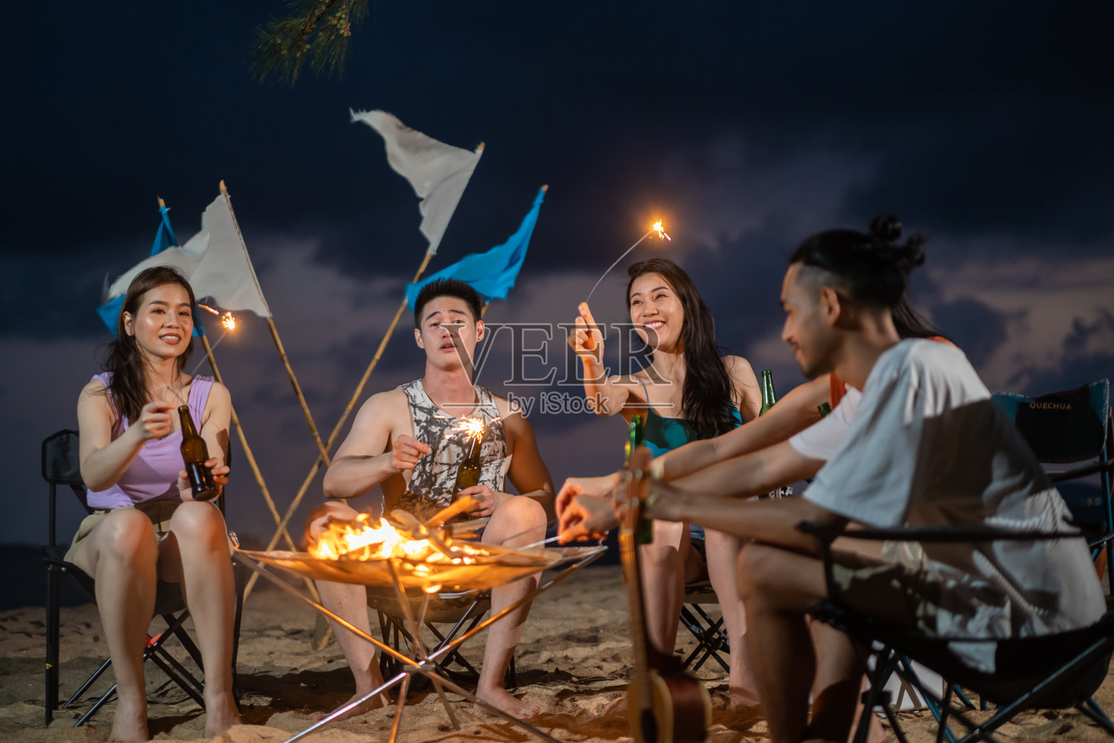 一群亚洲年轻男女晚上在海滩上聚会。迷人的朋友们在海边露营时唱歌跳舞，一起在热带海岛度假度假照片摄影图片