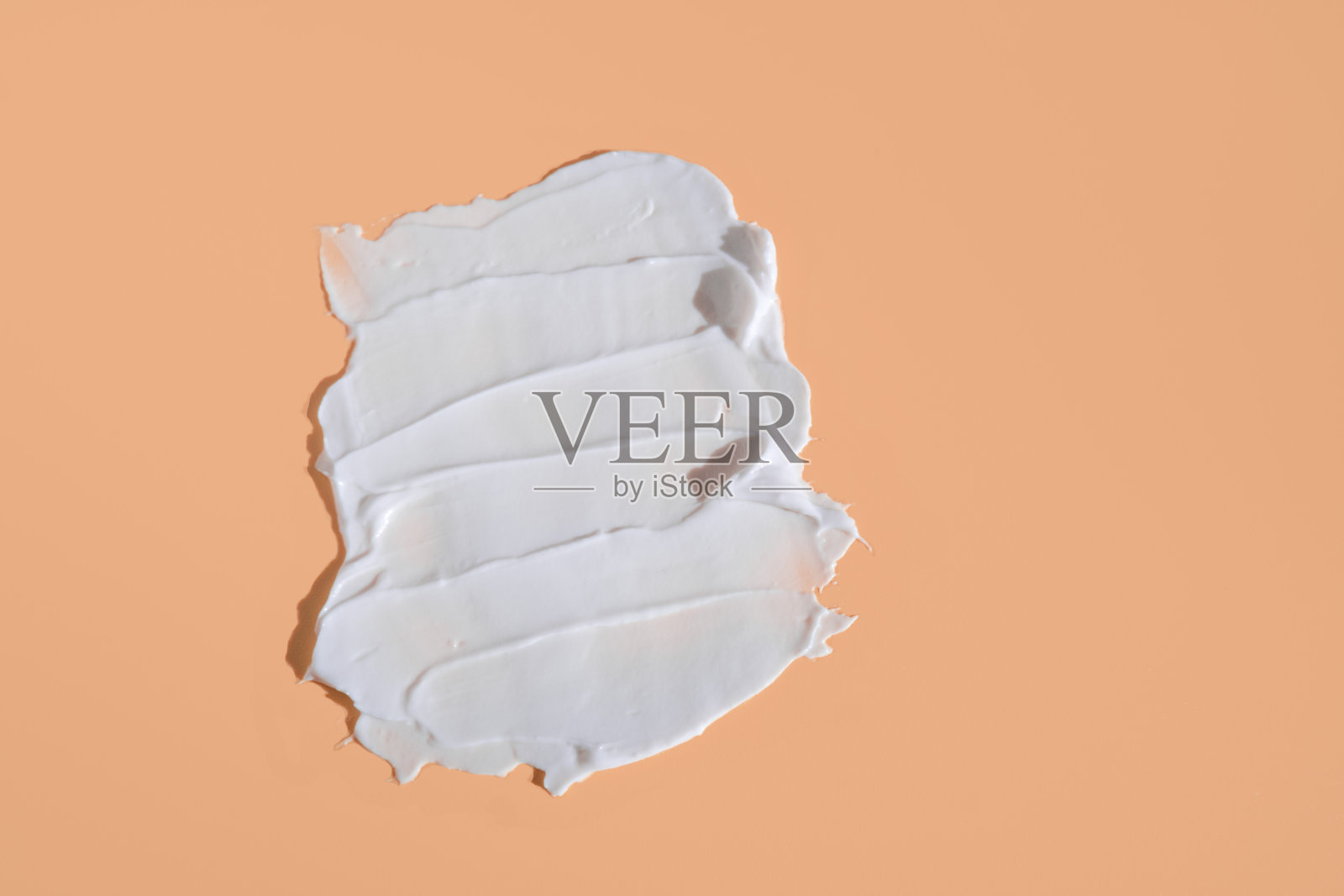 在米色背景上涂一层白色化妆品膏。分离出奶油粉底质地。涂抹面霜。奶油质地的特写照片摄影图片