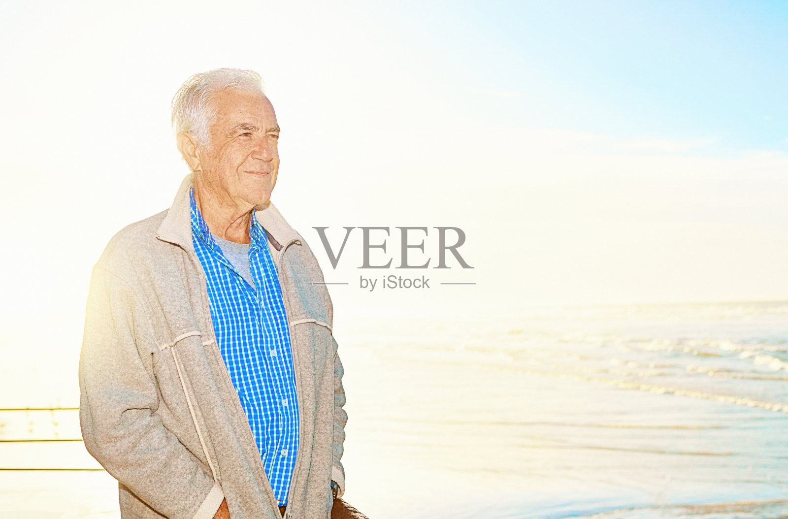 一位70多岁的英俊老人站在海边，双手插在口袋里，微笑着，看起来很满足照片摄影图片