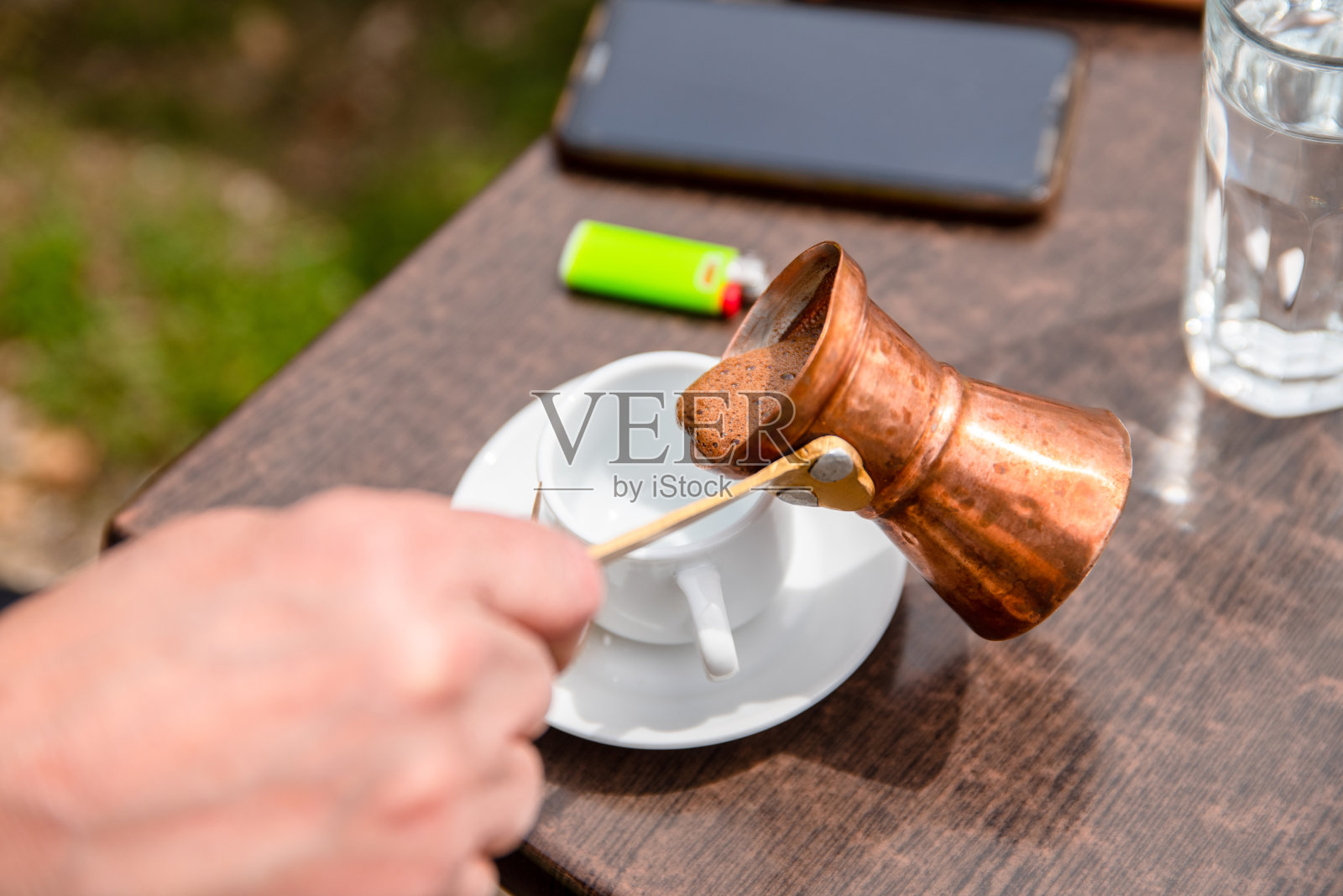 男子手从铜Cezve倒入桌子上的杯子传统希腊咖啡照片摄影图片