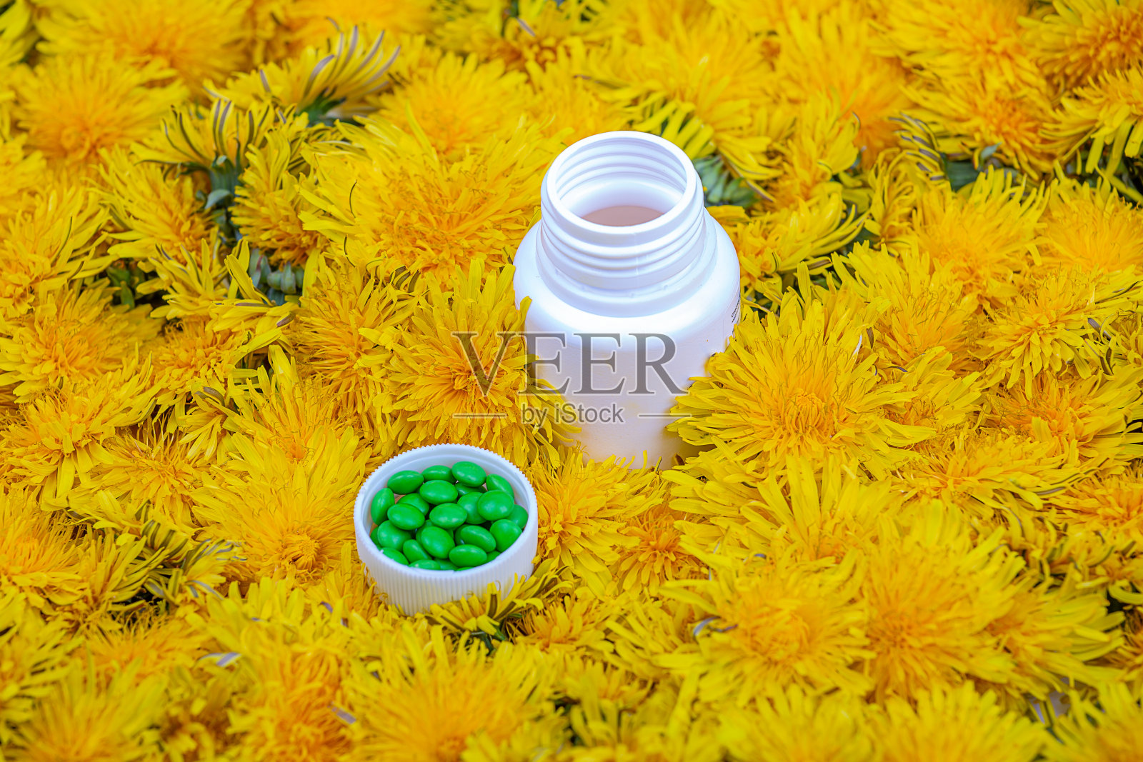 维生素在蒲公英。瓶子里装着蒲公英花里的绿色药丸，特写照片摄影图片