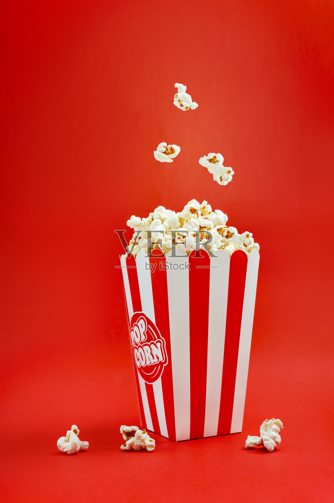 在红色背景的条纹纸板箱里，垂直落下的爆米花。爆米花悬浮。电影的时间。照片摄影图片