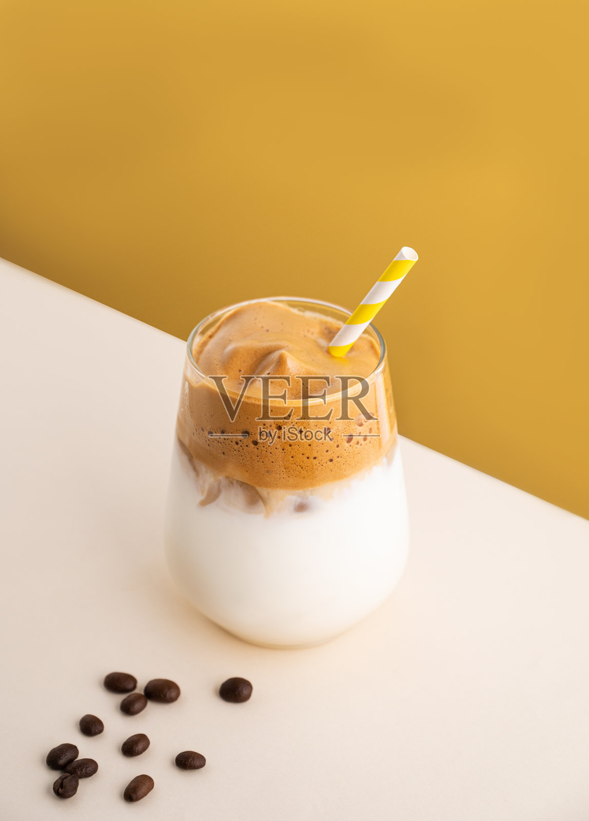 达尔戈纳咖啡加牛奶，杯子里放着冰块和黄色背景的谷物。夏日冷饮的概念。俯视图和复制空间。照片摄影图片