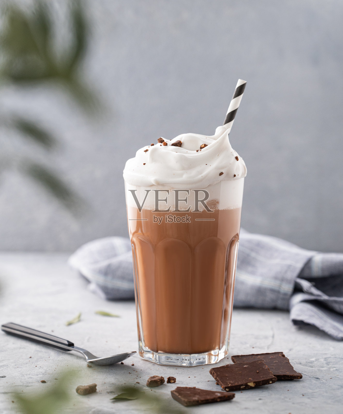 热巧克力，鲜奶油和巧克力碎片在一个高脚杯，蓝色的背景和一根树枝。正面视图和拷贝空间照片摄影图片