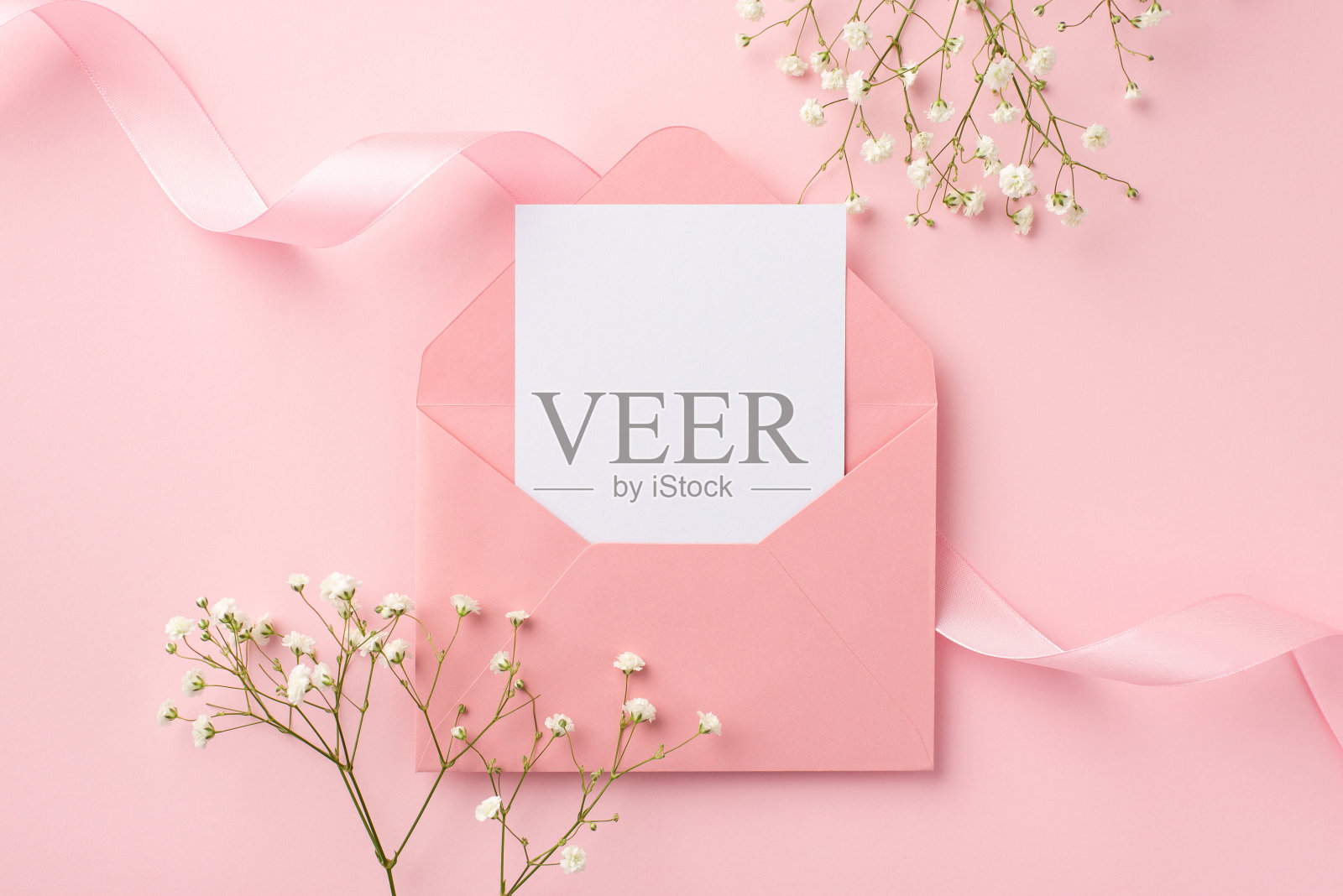 婚礼邀请的概念。顶视图照片开放的粉红色信封与纸卡粉红色卷丝带和白色的石膏花在孤立的粉彩粉红色背景与空白照片摄影图片