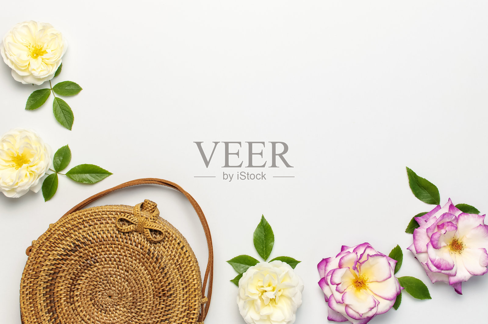 时尚概念的女性手袋。手工制作的天然有机藤条袋和精致的玫瑰花绿叶在光的背景。平铺，复制空间，俯视图。从巴厘岛Ecobags。照片摄影图片