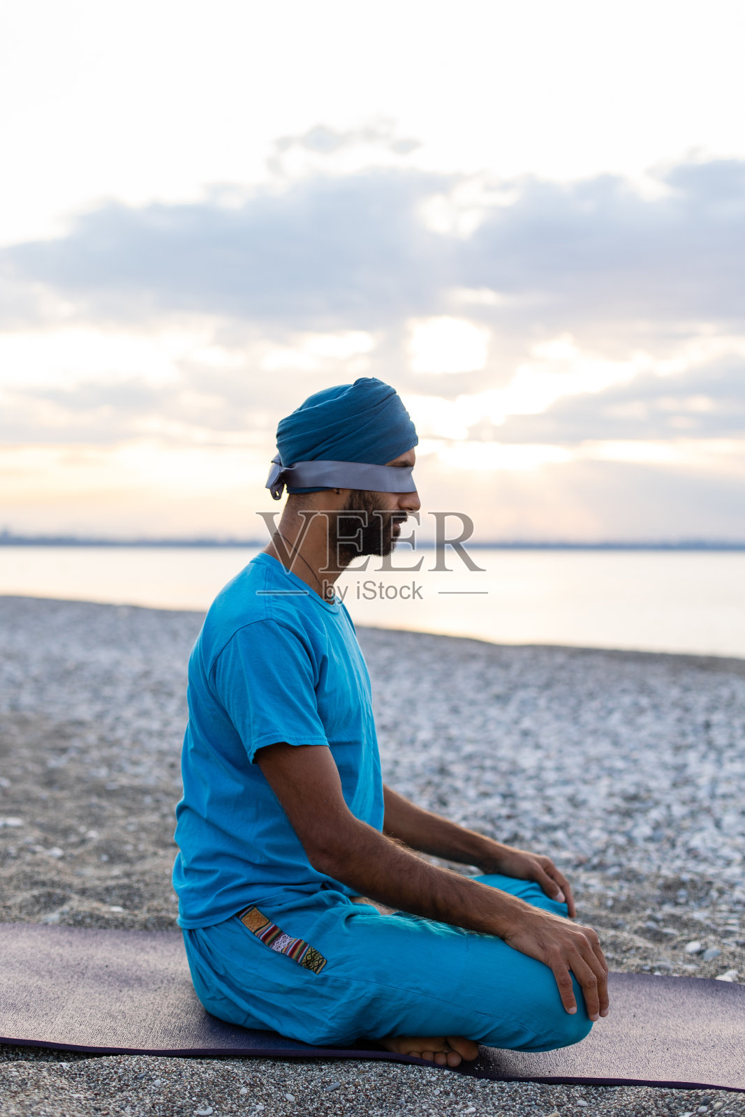 一个健康的年轻人坐在海边，摆着瑜伽莲花的姿势，在日出的沙滩上冥想。照片摄影图片