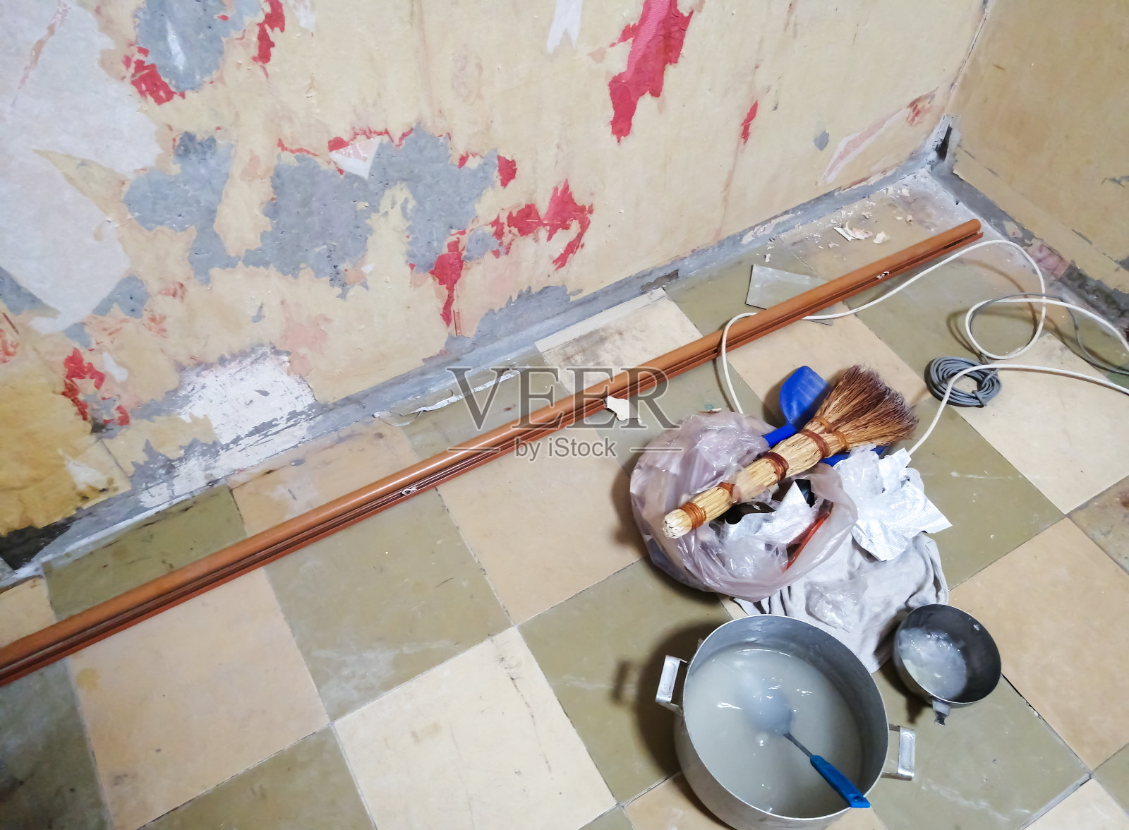 公寓装修。脏墙后的墙纸剥落，壁纸用焊胶，扫把，摩丝放在地板上。照片摄影图片