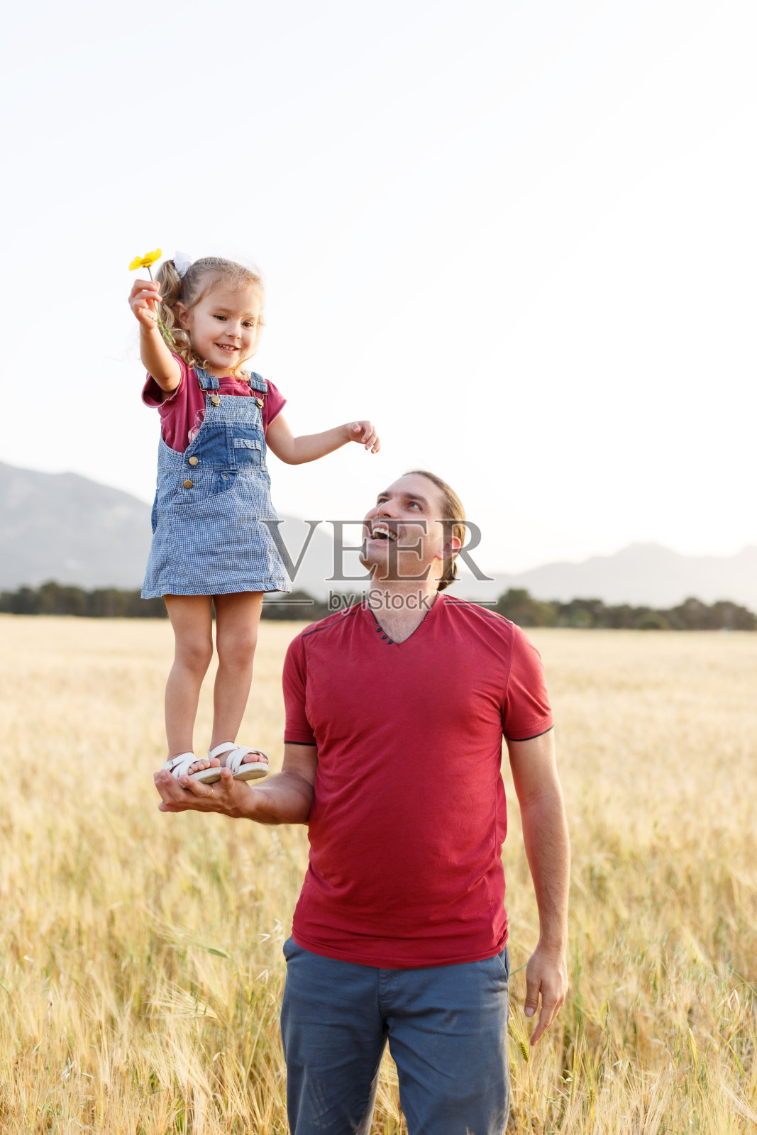快乐的父亲抱着他的女儿玩耍。成熟的男人和他的小女儿在大自然中玩耍。微笑快乐的父亲和女儿在公园里玩耍，拥抱她。照片摄影图片