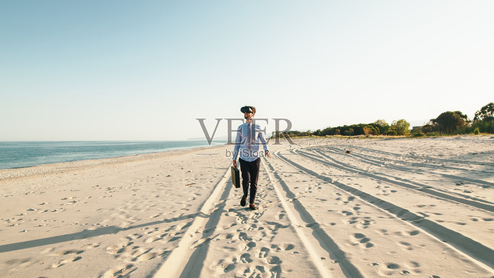 戴VR眼镜在海滩上行走的商务人士照片摄影图片