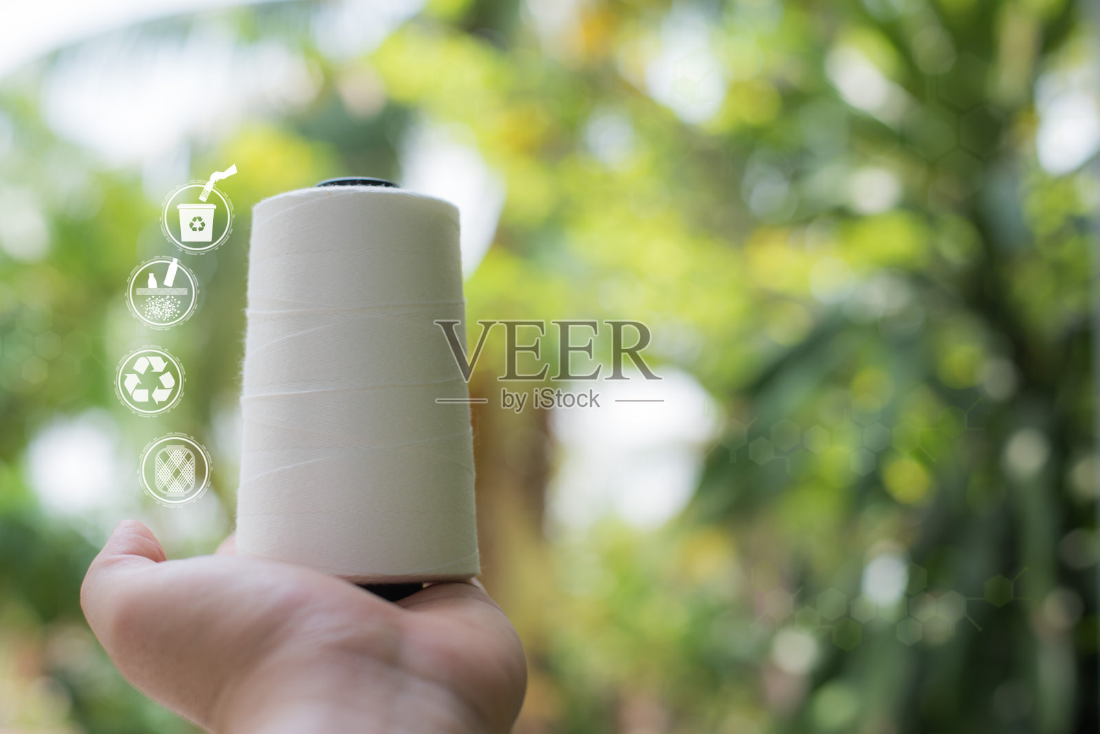 手持式原白涤纶FDY纱芯，涤纶长丝纱芯。聚酯纤维纱线，涤纶缝纫线与模糊的绿色背景。回收图标，可持续图标和瓶子图标照片摄影图片