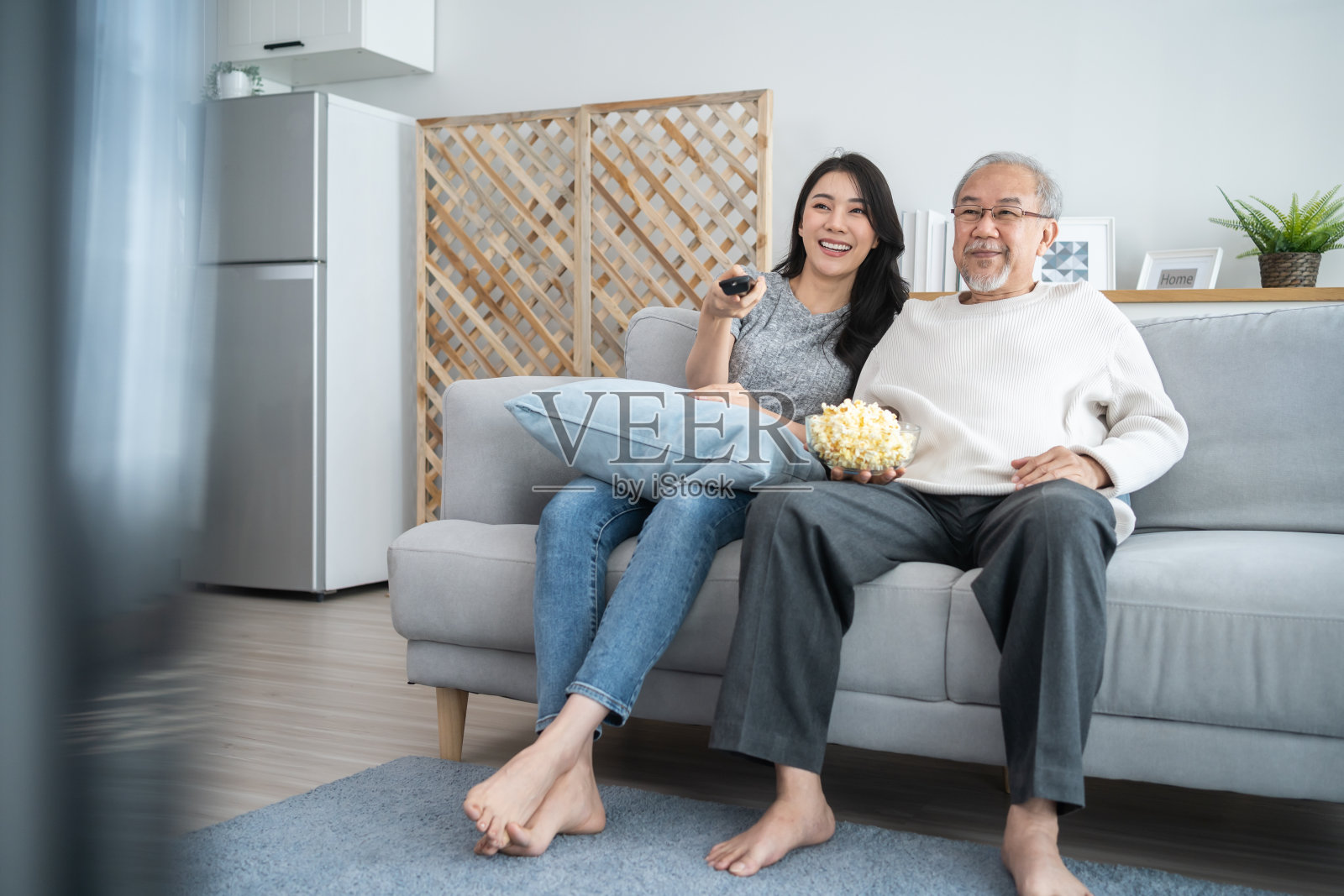 亚洲年长的成熟男人和年轻的女儿坐在沙发上看电影。迷人的漂亮女孩花时间与年迈的父亲享受喜剧节目，在家里的客厅一起吃爆米花照片摄影图片