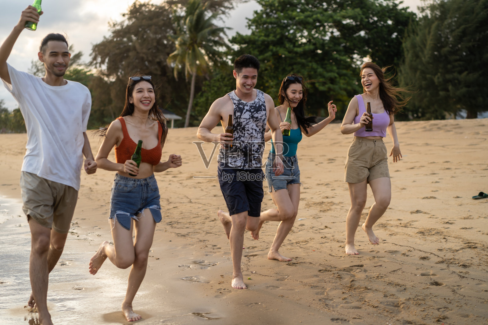 一群亚洲年轻男女在海滩上聚会。迷人的朋友唱歌、跳舞，在海边散步、跑步，在热带海岛享受假期度假之旅。照片摄影图片