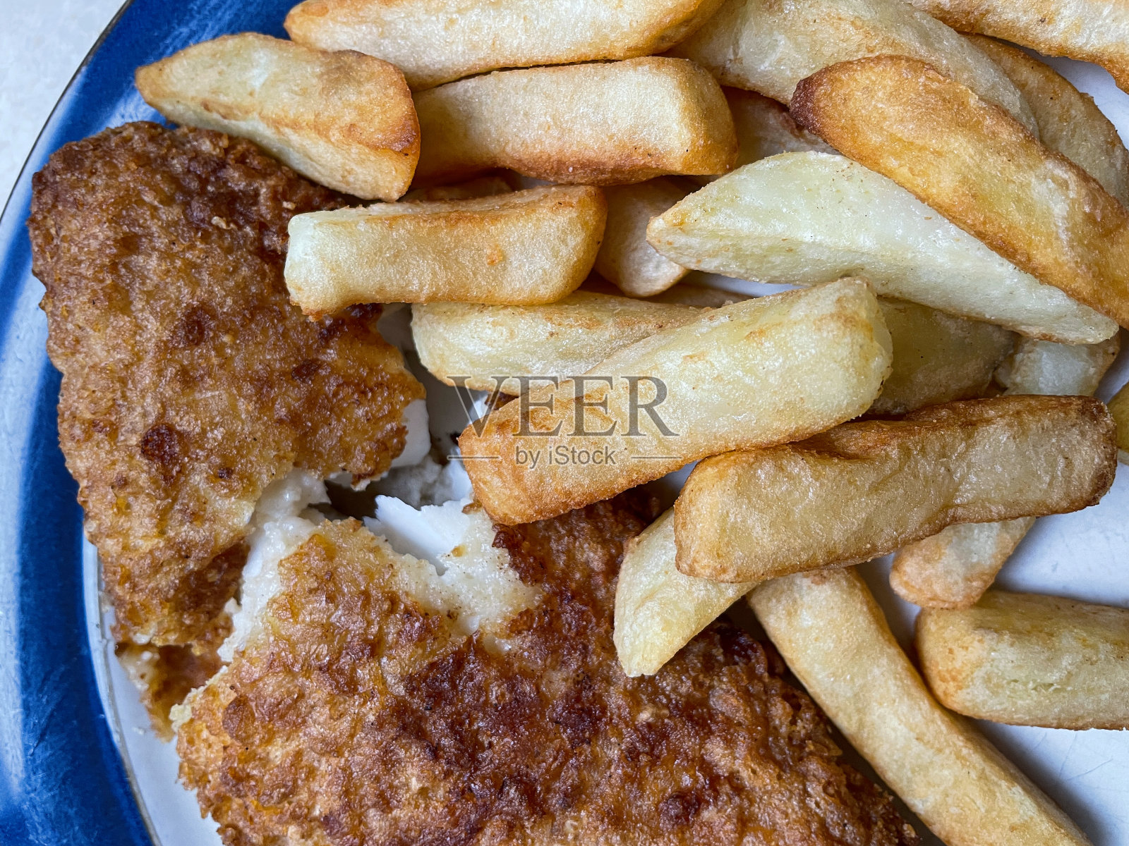 全帧图像的蓝色镶边盘子包含片状的白色鱼和薯条，啤酒脆鳕鱼和土豆楔形，提高的观点照片摄影图片