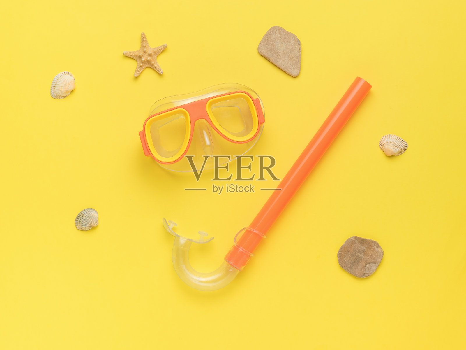 橙色的通气管和游泳面罩，黄色的背景，石头和贝壳。水肺潜水和夏季休闲的最小概念。照片摄影图片