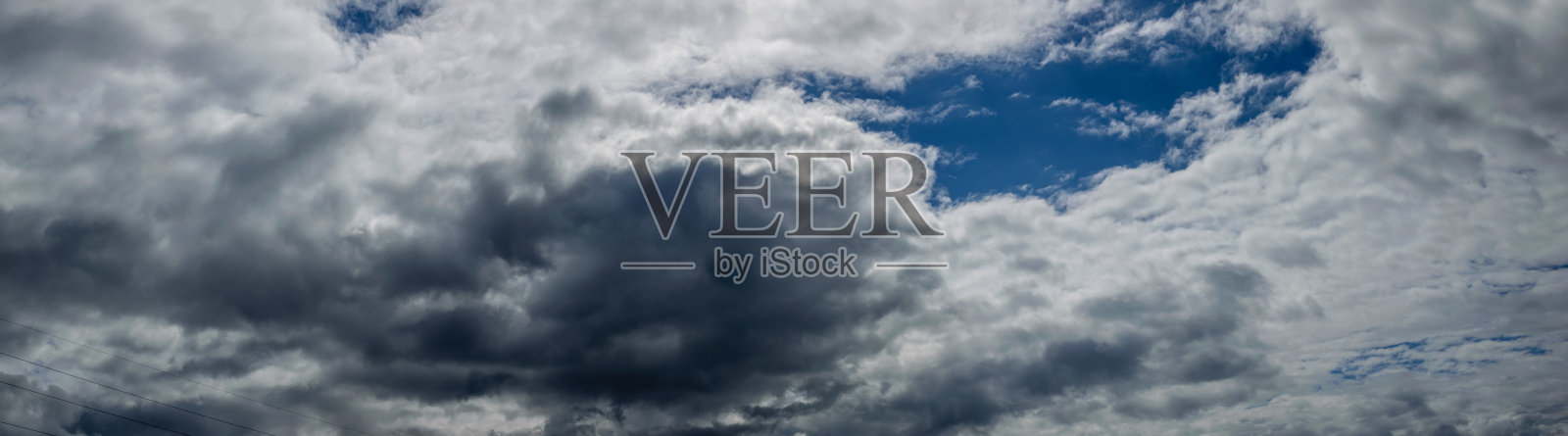 蓝色天空下蓬松的白色和深灰色积云的全景图。照片摄影图片