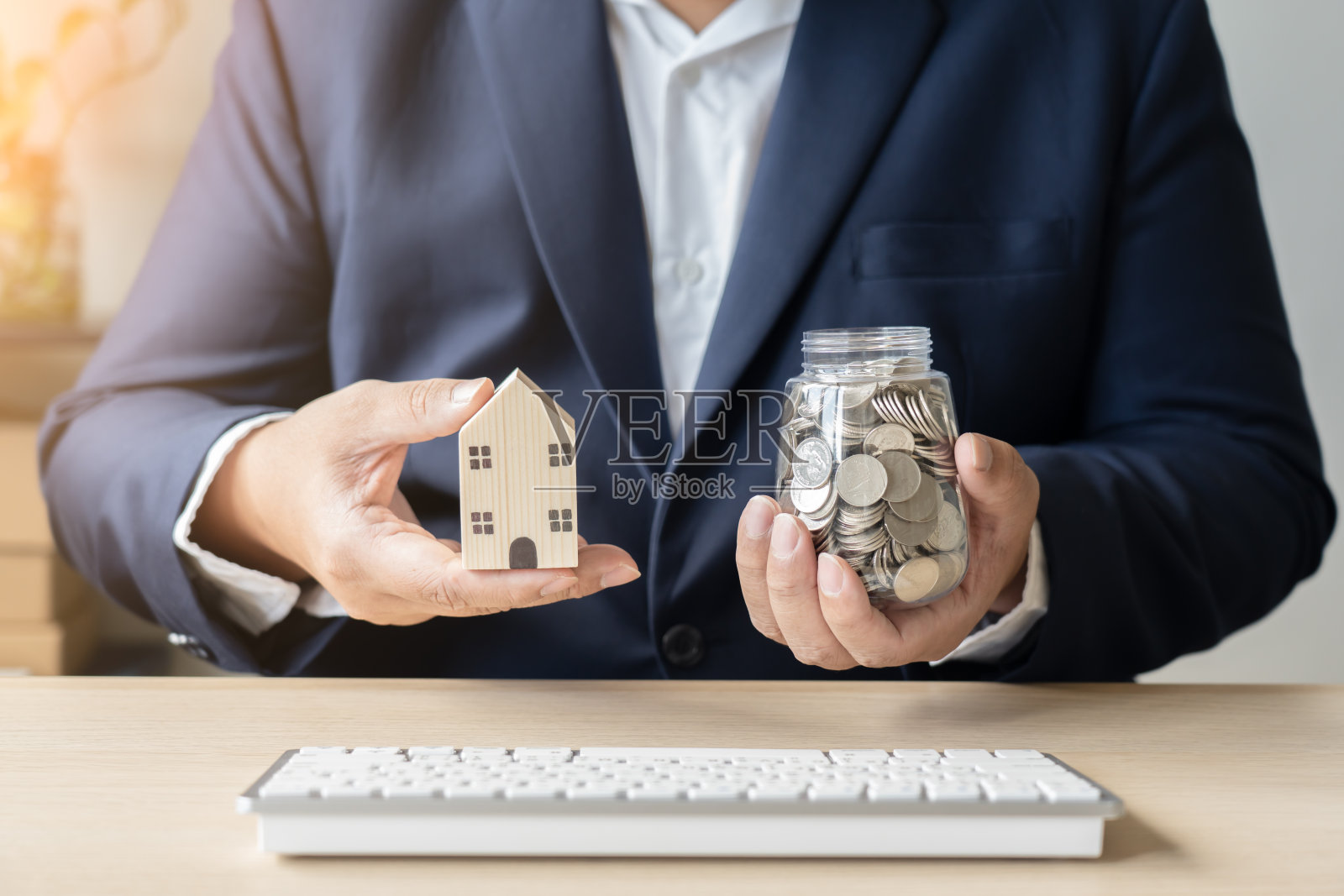 商人使用笔记本电脑存钱，泰币硬币在罐子里用于买房照片摄影图片