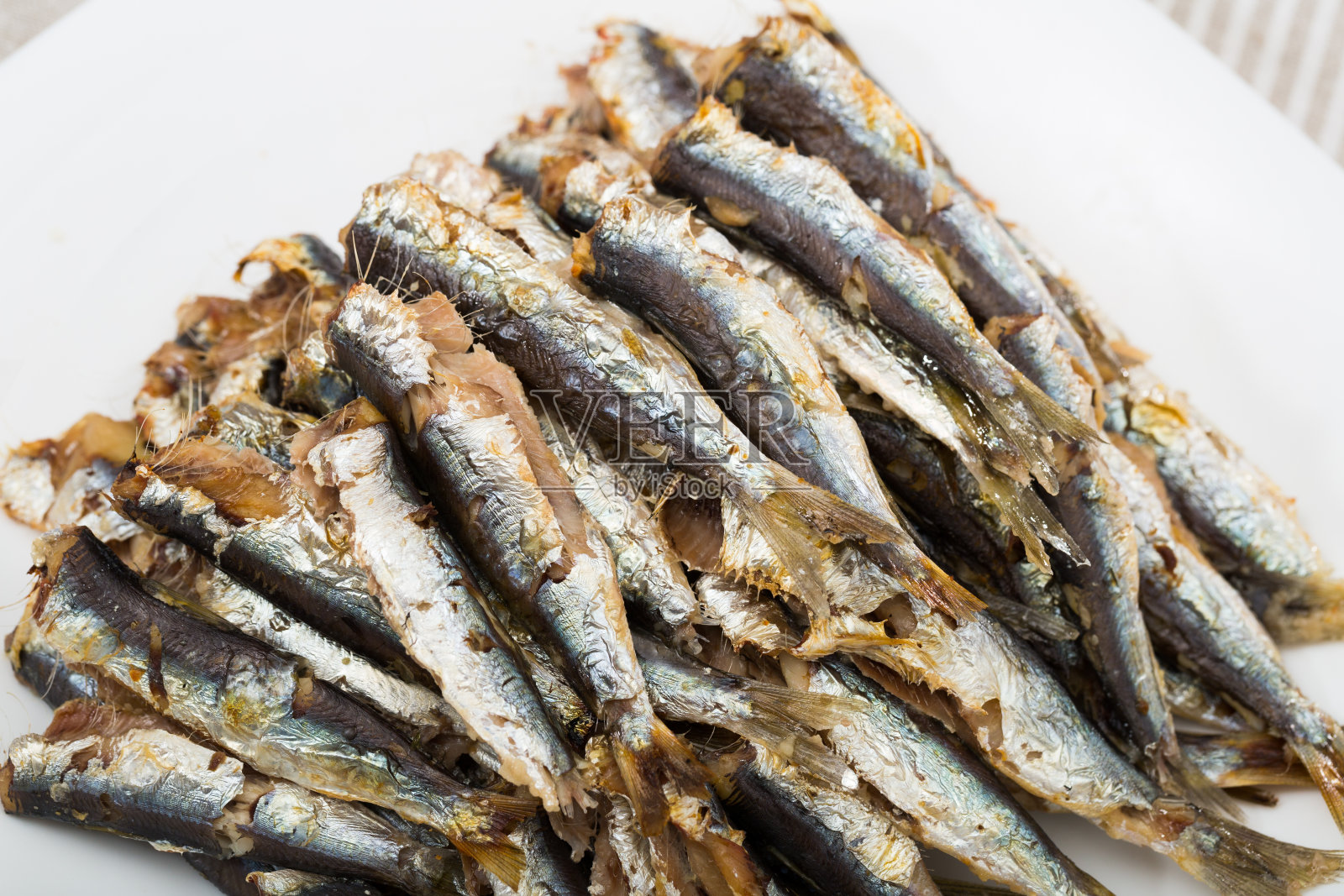 美味的烤小鲱鱼盛在餐桌的白色盘子里照片摄影图片