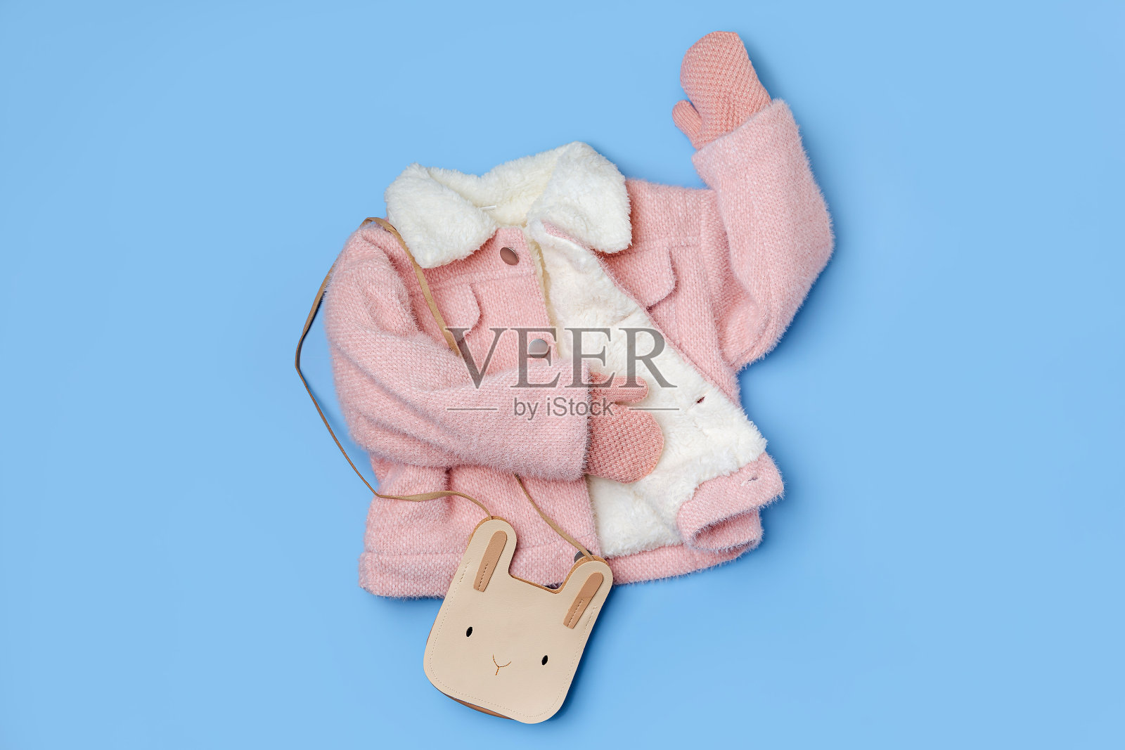 儿童粉红色皮草外套，蓝色背景可爱的包。时尚儿童外套。冬季时尚服装照片摄影图片