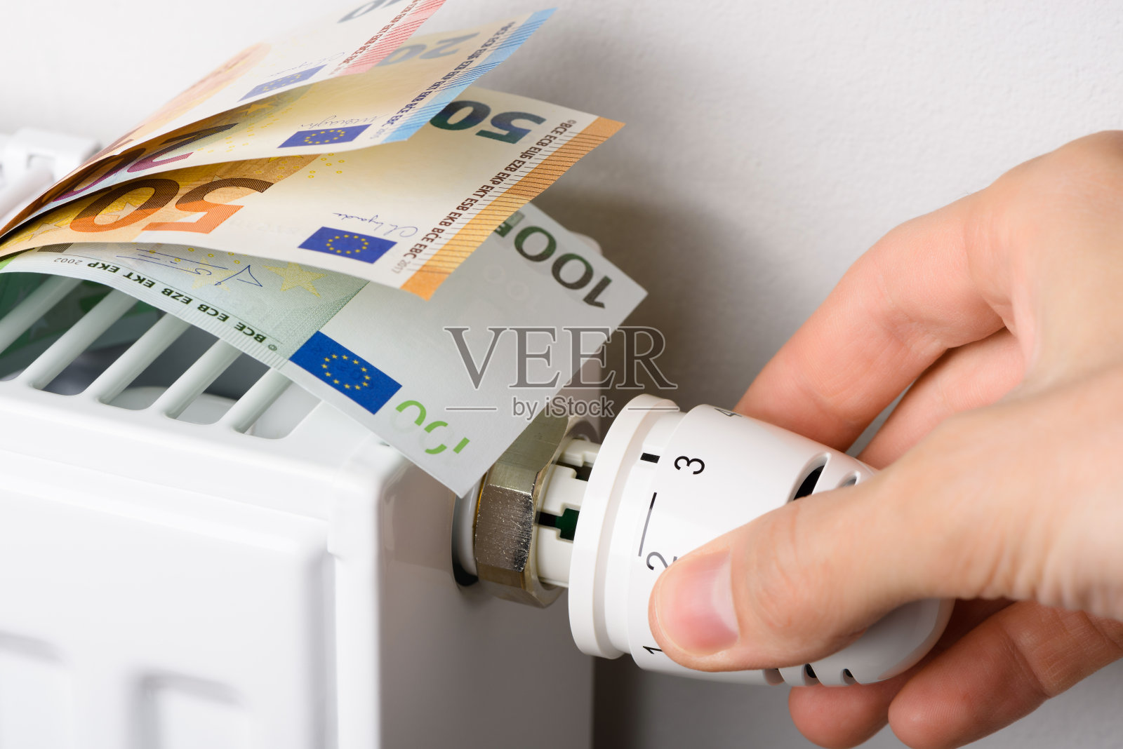 用手调节装有欧元钞票的暖气片温控器的阀门旋钮照片摄影图片
