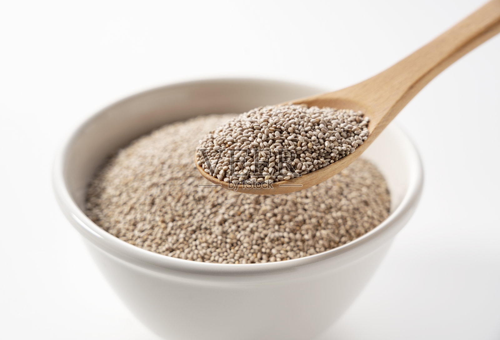 白色的奇亚籽放在白色的碗里，衬着白色的背景。用木勺舀。照片摄影图片