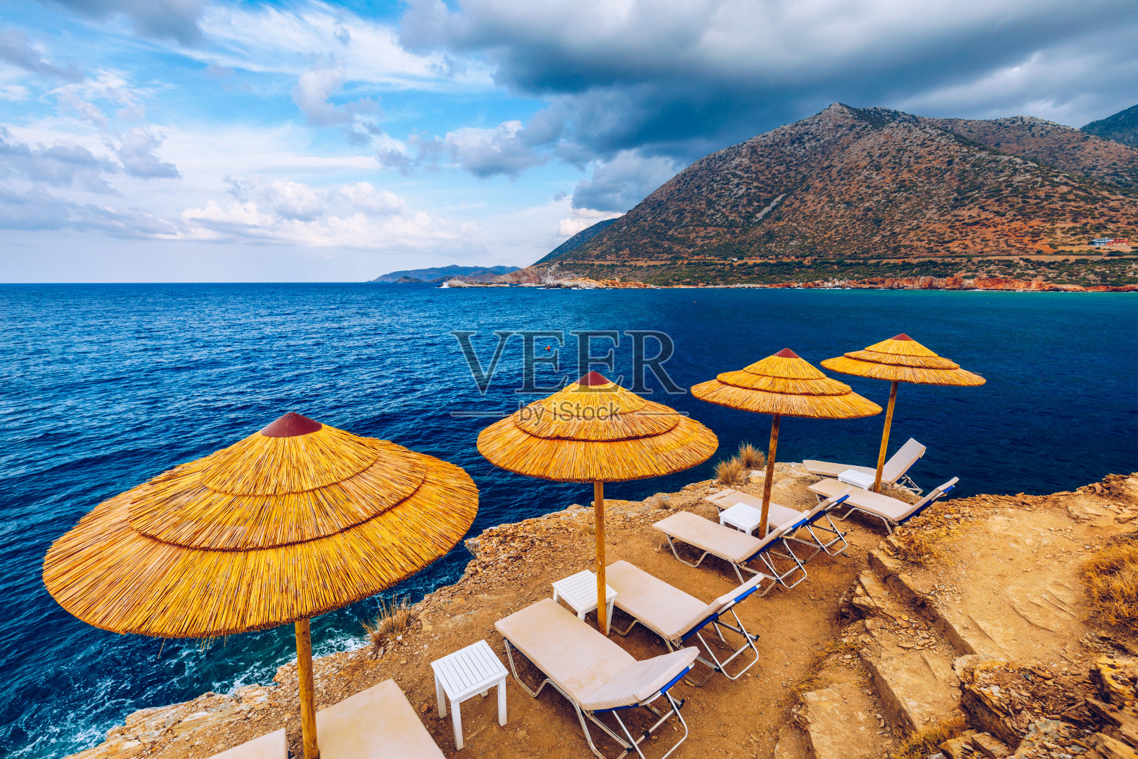 暑假的目的地。稻草遮阳伞和日光浴床在空旷的卵石海滩上，背景是大海。度假和旅游概念。天堂海滩上的日光浴床。伞,日光浴浴床。照片摄影图片