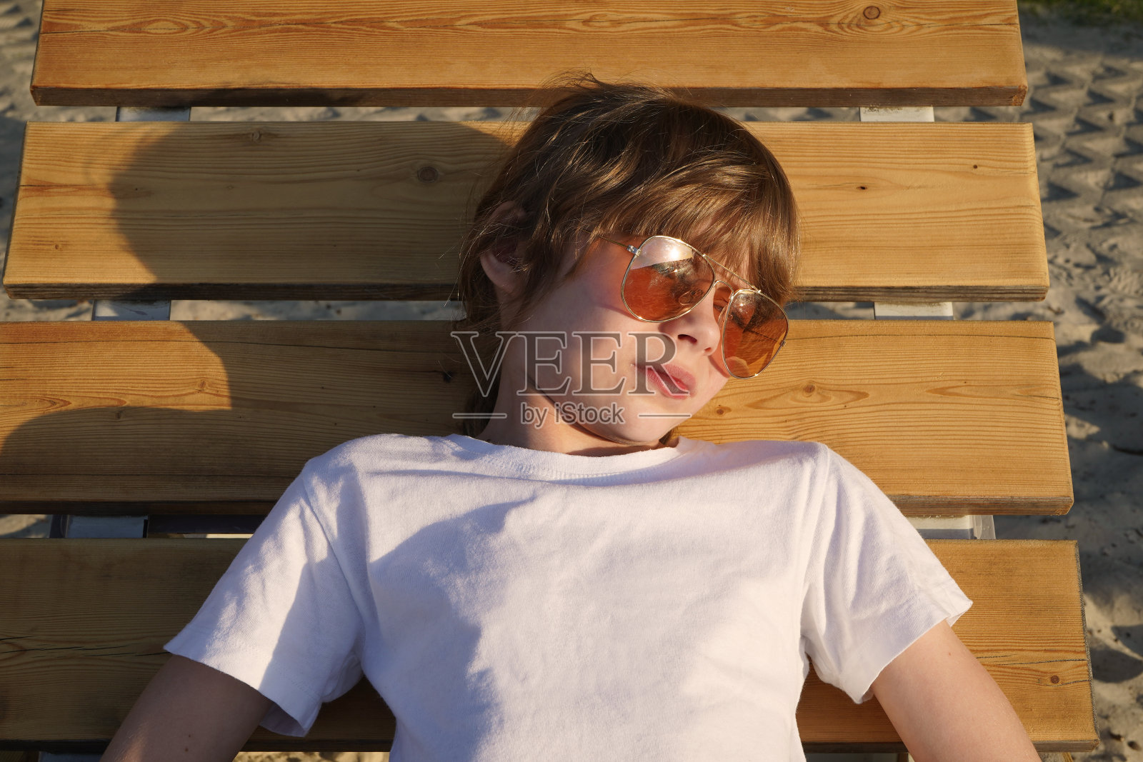 女孩戴着粉色眼镜，坐在海滩的木制躺椅上照片摄影图片