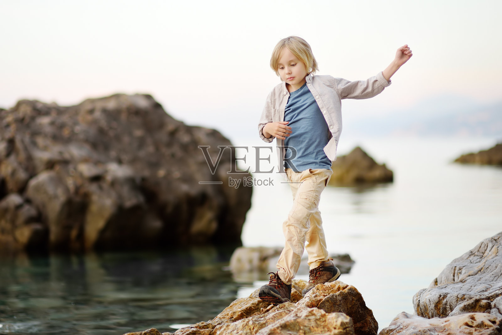 可爱的学童在海边的岩石边远足，玩得开心，探索自然。照片摄影图片
