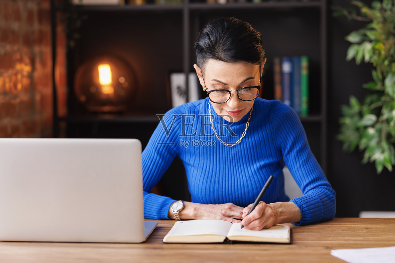 中年女商人在笔记本电脑上工作，在家做笔记照片摄影图片