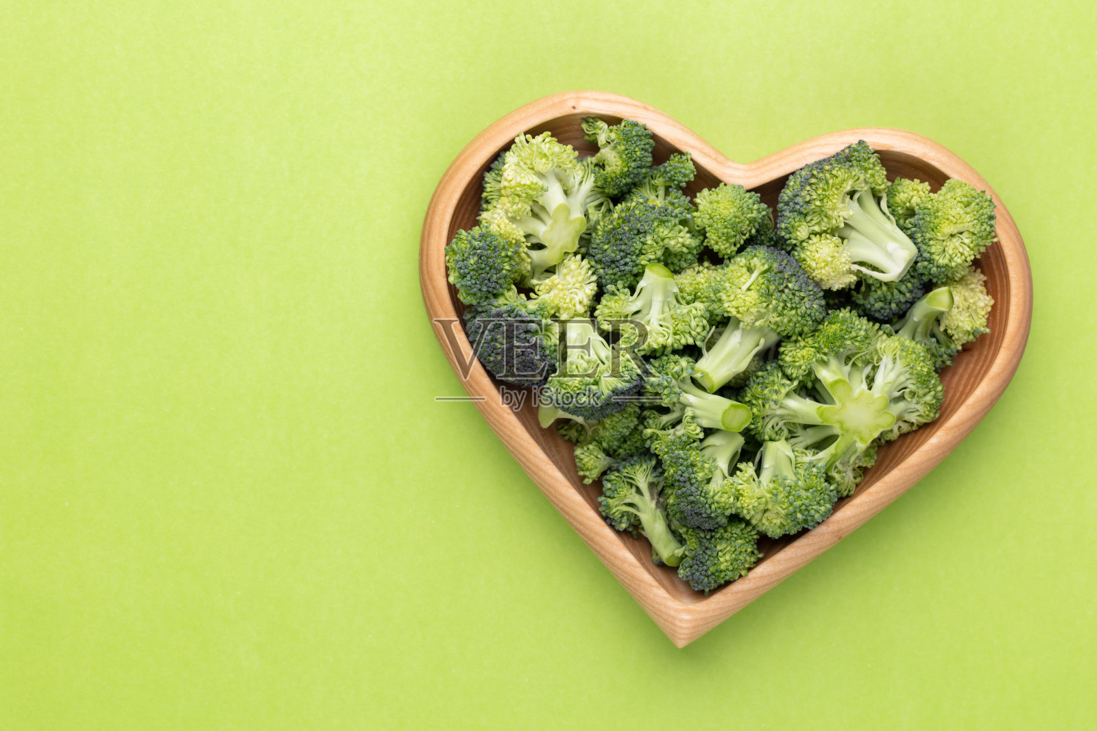 新鲜的花椰菜放在心形的碗里，放在木制的背景上。照片摄影图片