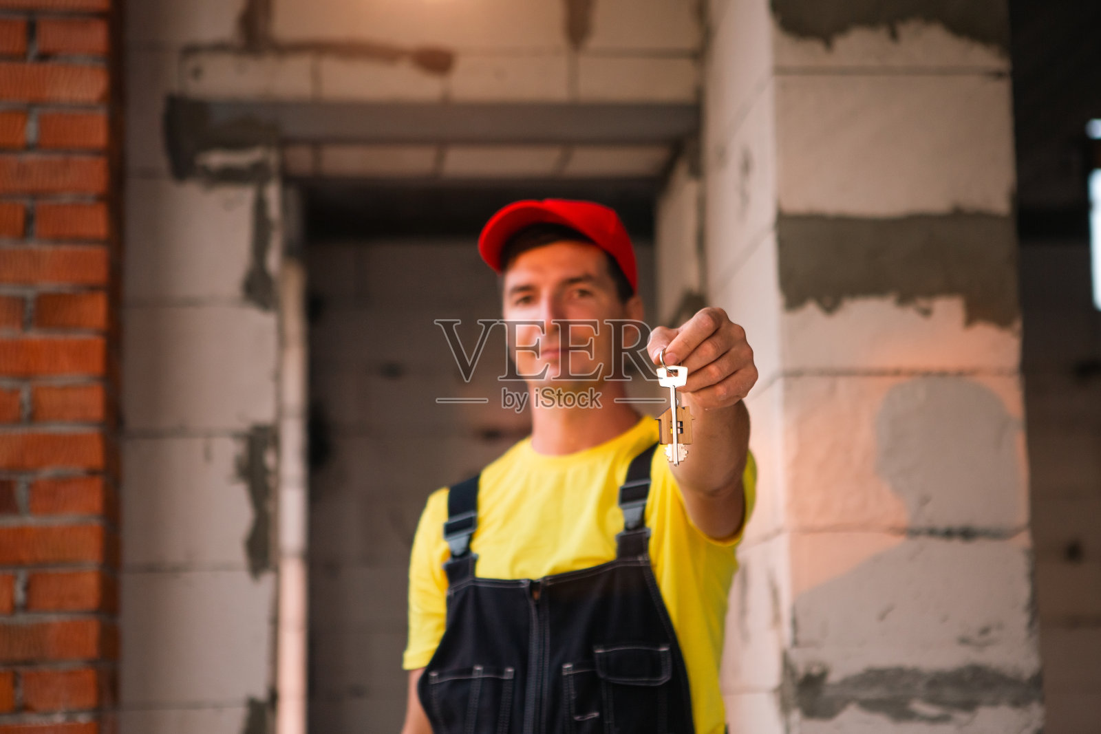 建筑工地的建筑工人工程师用卷尺测量窗洞和砖墙的长度。穿着工作服的男人，连身裤和帽子照片摄影图片